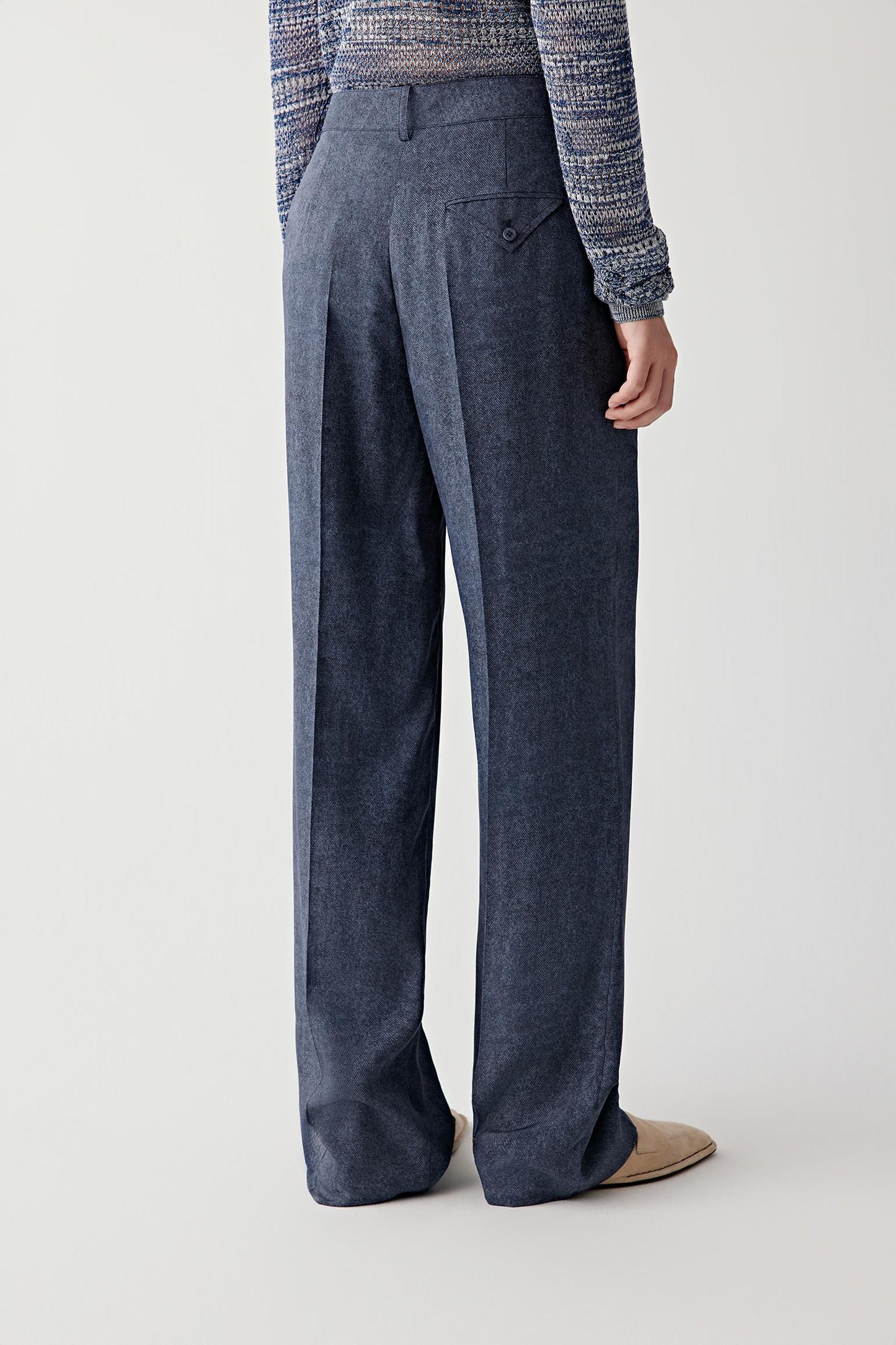 Three-quarter back view showing the clean rear construction, straight-leg line and fluid movement through the trousers, with the fabric maintaining a soft structured fall