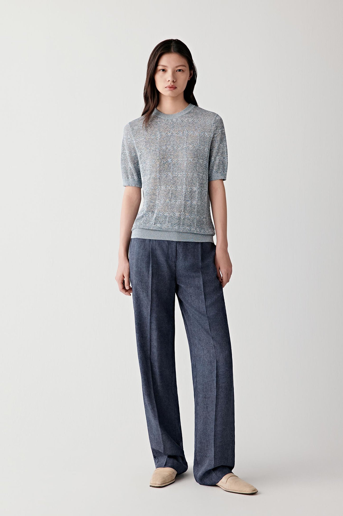 Full-length front view of a woman wearing indigo blue silk twill straight-leg trousers paired with a striped knit top, highlighting the structured waistband, straight-leg cut and fluid drape of the lightweight silk fabric