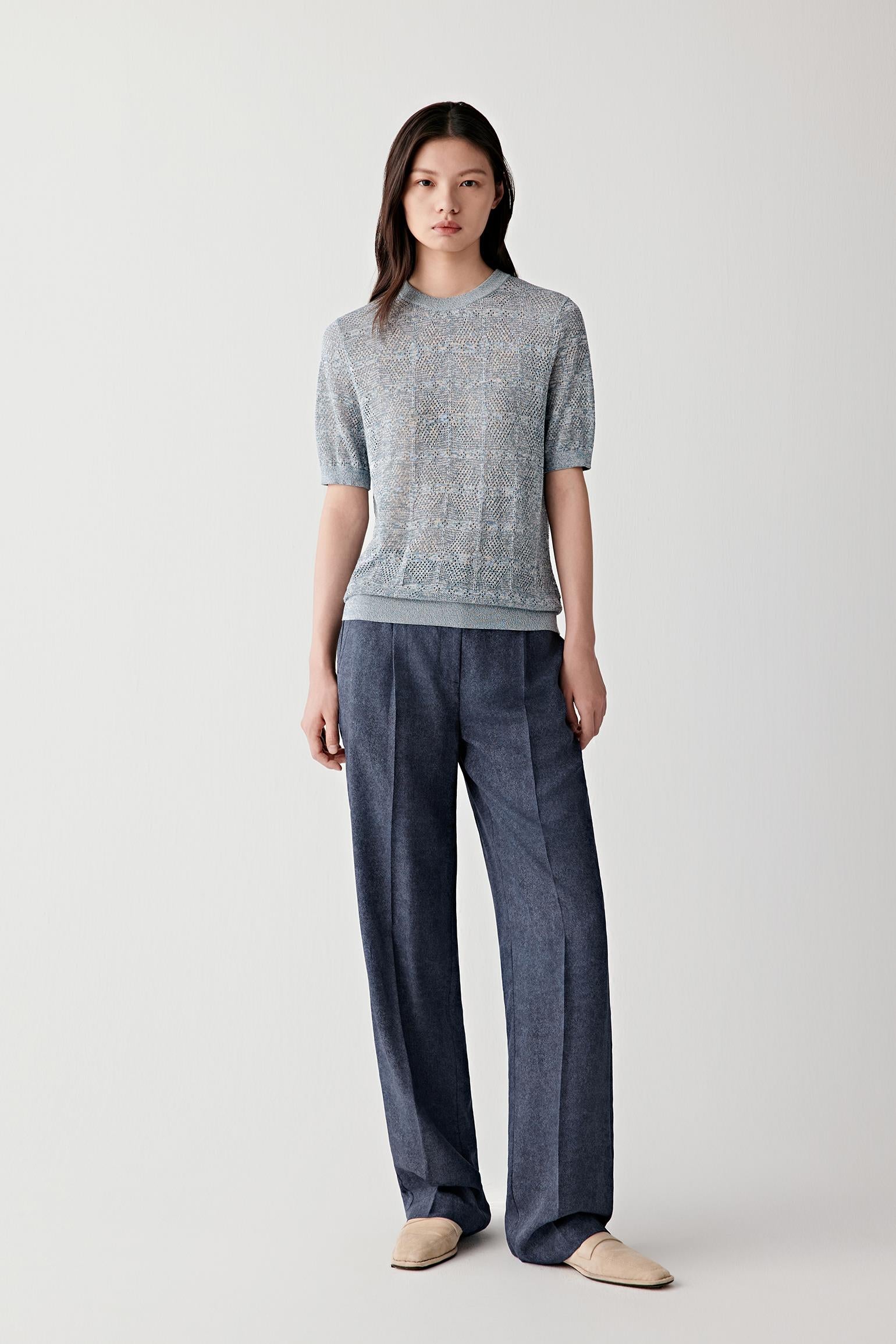 Full-length front view of a woman wearing indigo blue silk twill straight-leg trousers paired with a striped knit top, highlighting the structured waistband, straight-leg cut and fluid drape of the lightweight silk fabric