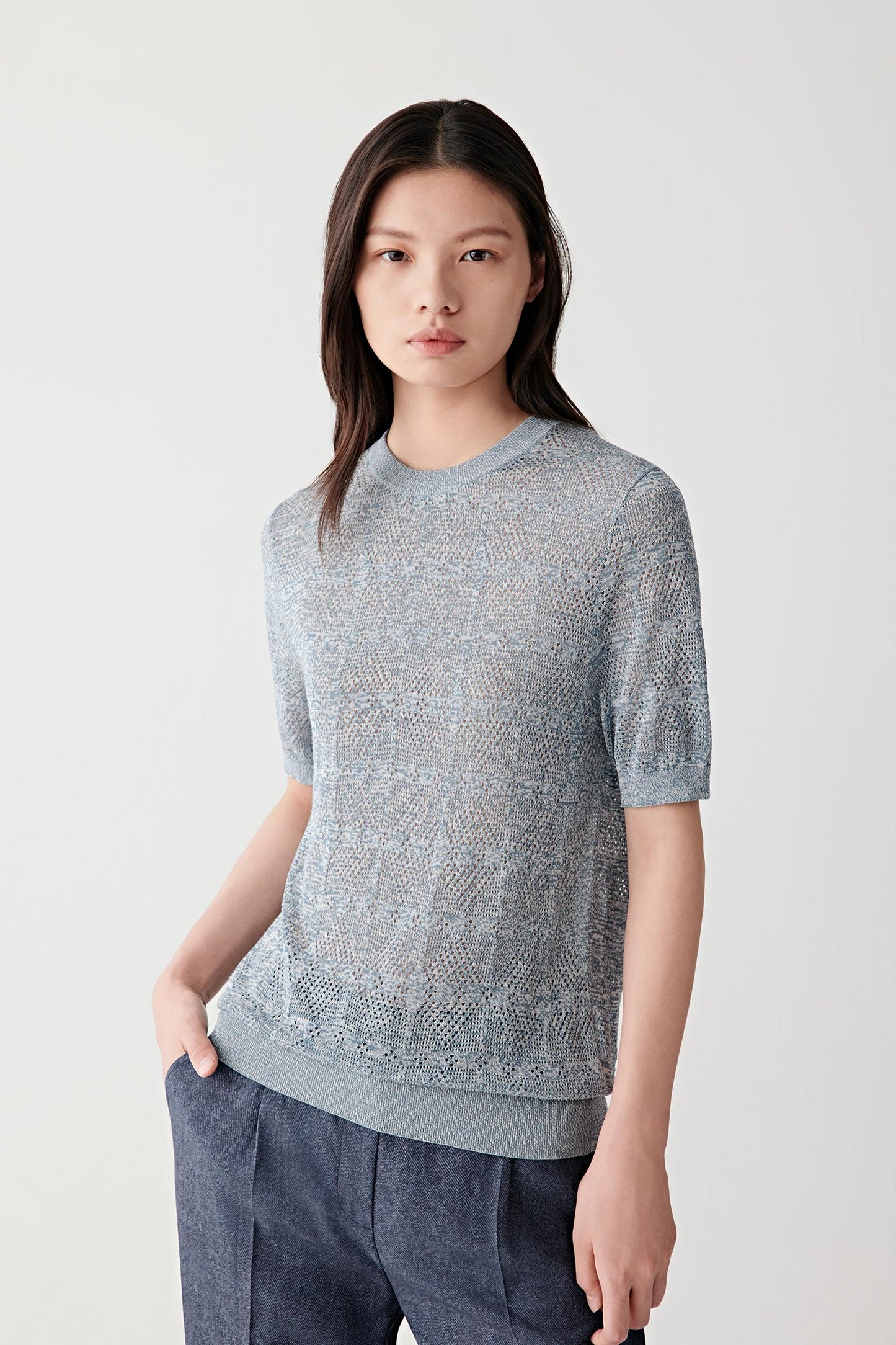 Front view of a woman wearing a blue and white melange cotton and silk pullover with short sleeves, highlighting the lightweight openwork knit texture, relaxed silhouette and softly textured dry surface