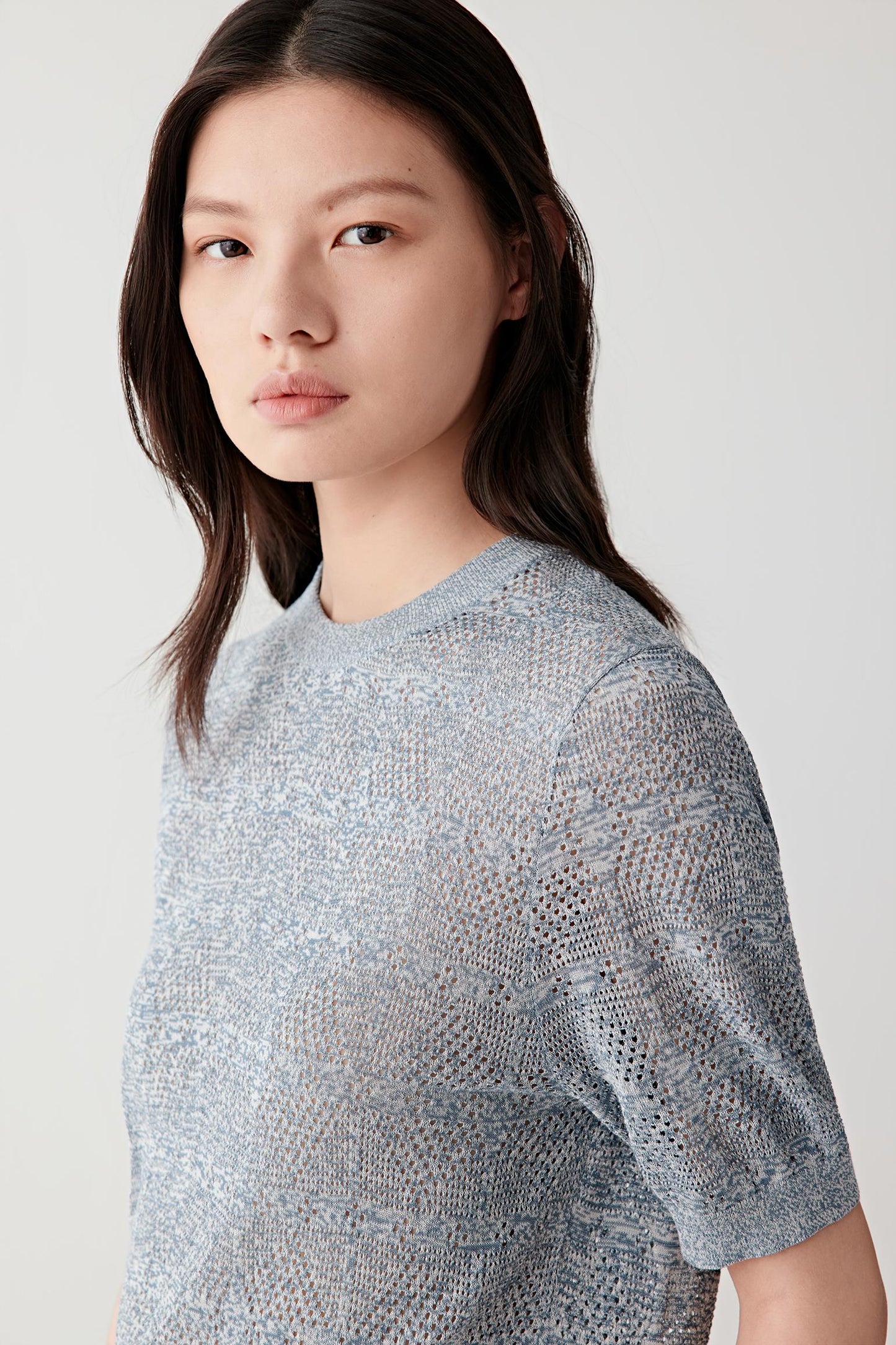 Close-up portrait focusing on the neckline and knit structure, detailing the lightly textured openwork surface and the blended blue and white melange coloration