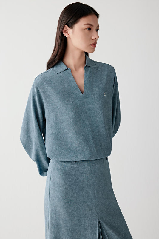 Three-quarter front view of a woman wearing an indigo blue silk crêpe de Chine blouse with a fluid silhouette and soft drape, highlighting the lightweight texture, softly structured shoulders and fluid movement of the fabric across the body