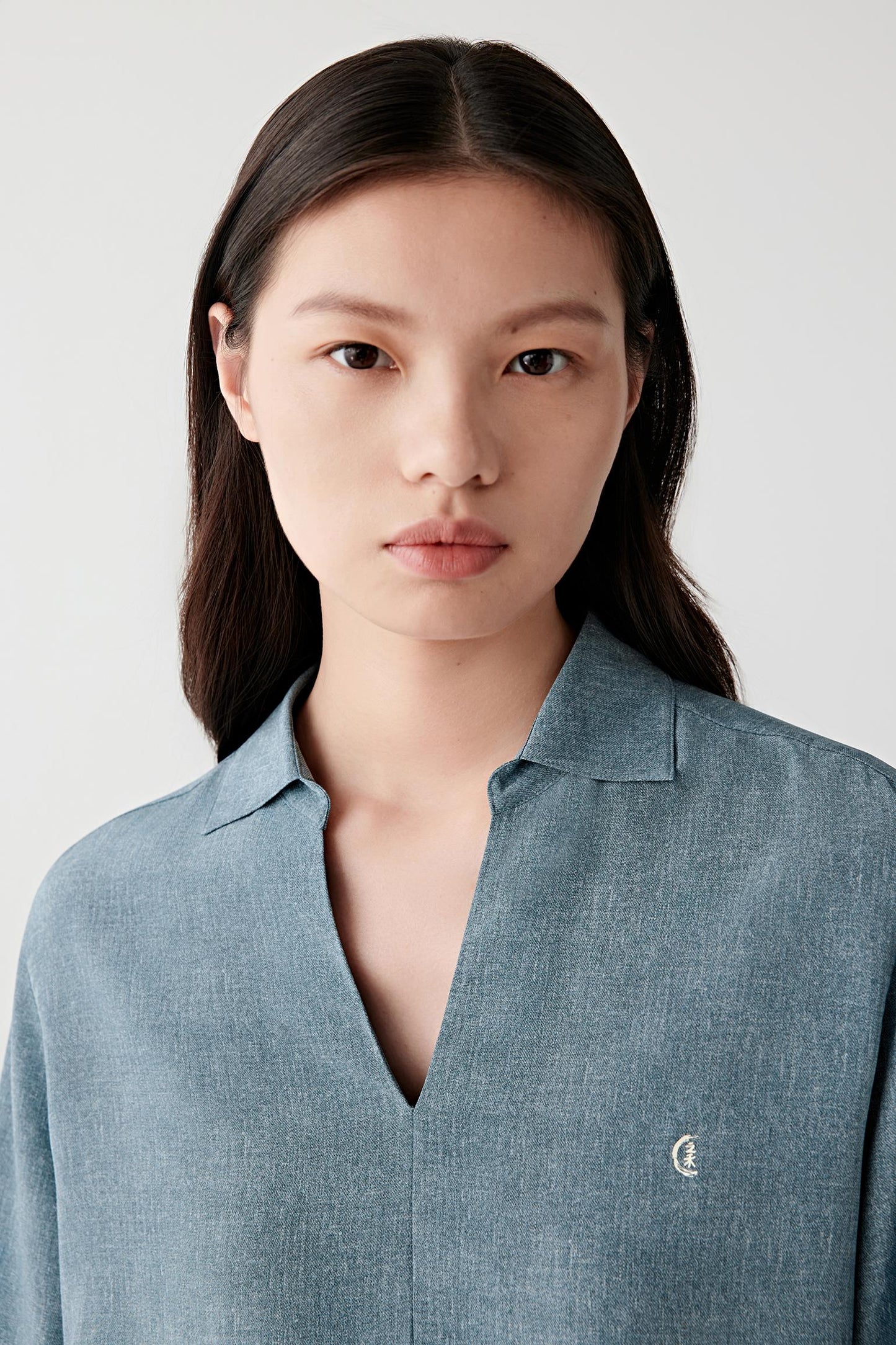 Close-up portrait focusing on the neckline and concealed placket, detailing the soft open collar, tonal button fastening and lightly textured silk surface with subtle depth and fluidity