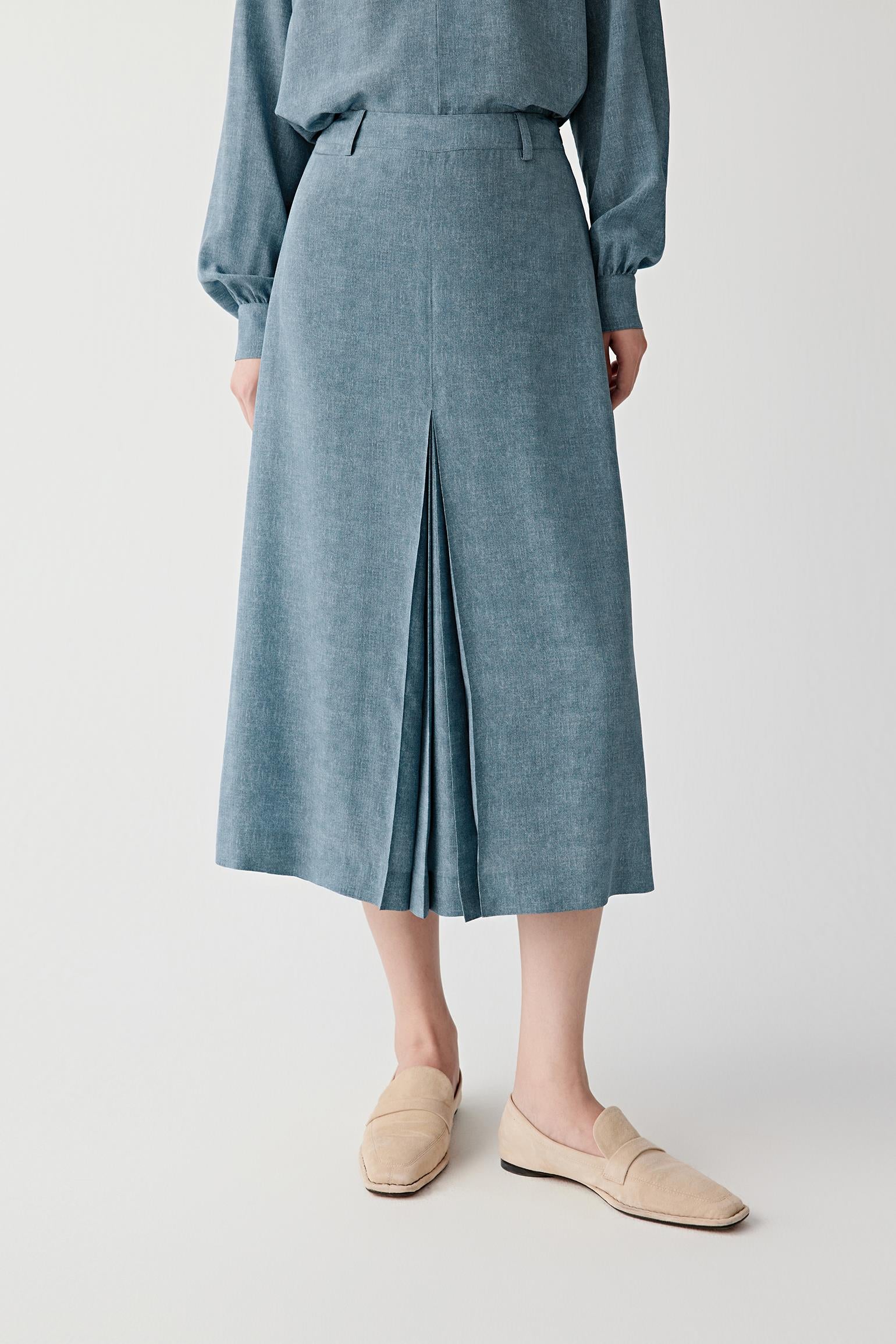Mid-length front view focusing on the pleated construction and lower silhouette, emphasizing the structured front pleat, fluid movement and softly flowing texture of the indigo blue silk crêpe de Chine