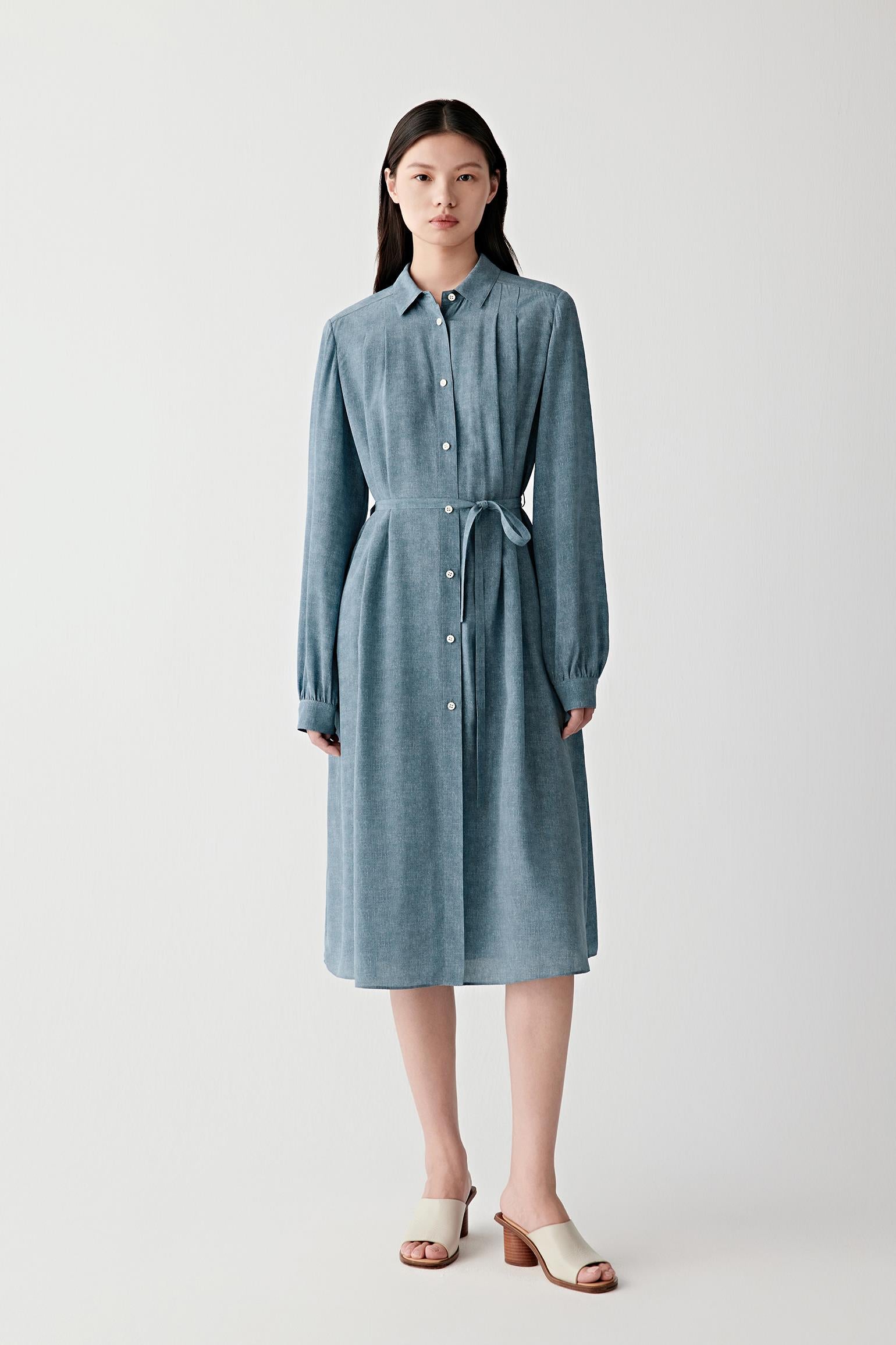Full-length front view of a woman wearing an indigo blue silk crêpe de Chine belted dress with a fluid silhouette, highlighting the pointed collar, concealed button placket and softly draped fabric with subtle depth