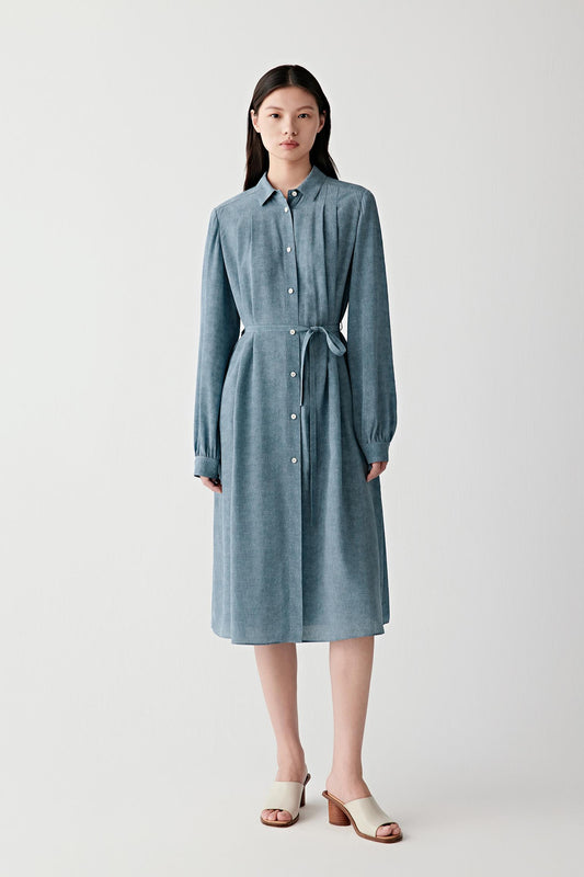 Full-length front view of a woman wearing an indigo blue silk crêpe de Chine belted dress with a fluid silhouette, highlighting the pointed collar, concealed button placket and softly draped fabric with subtle depth