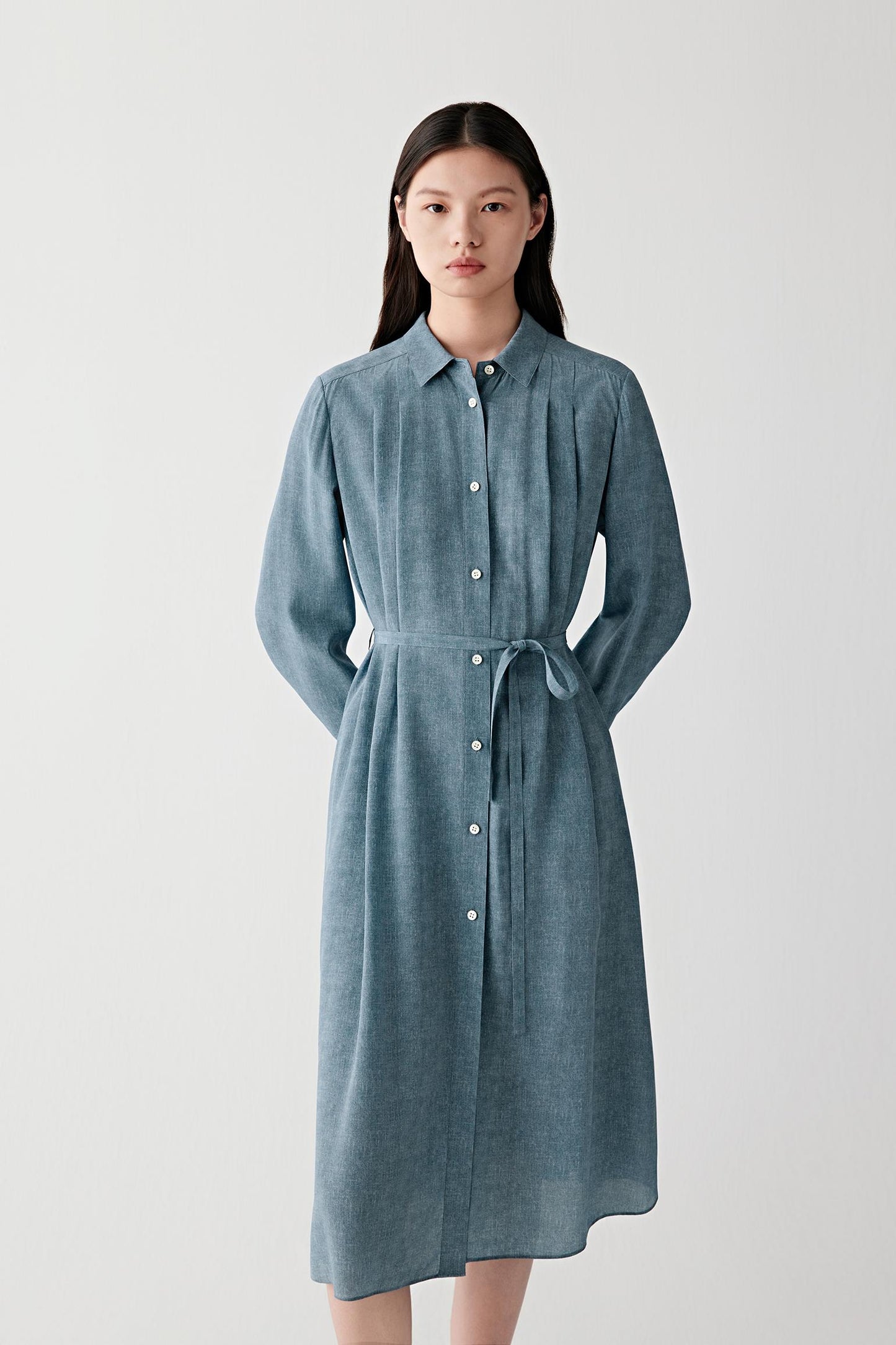 Mid-length front view emphasizing the self-tie belt, softly gathered waist and fluid drape of the skirt, with the indigo blue tone revealing tonal variation and a matte silk surface