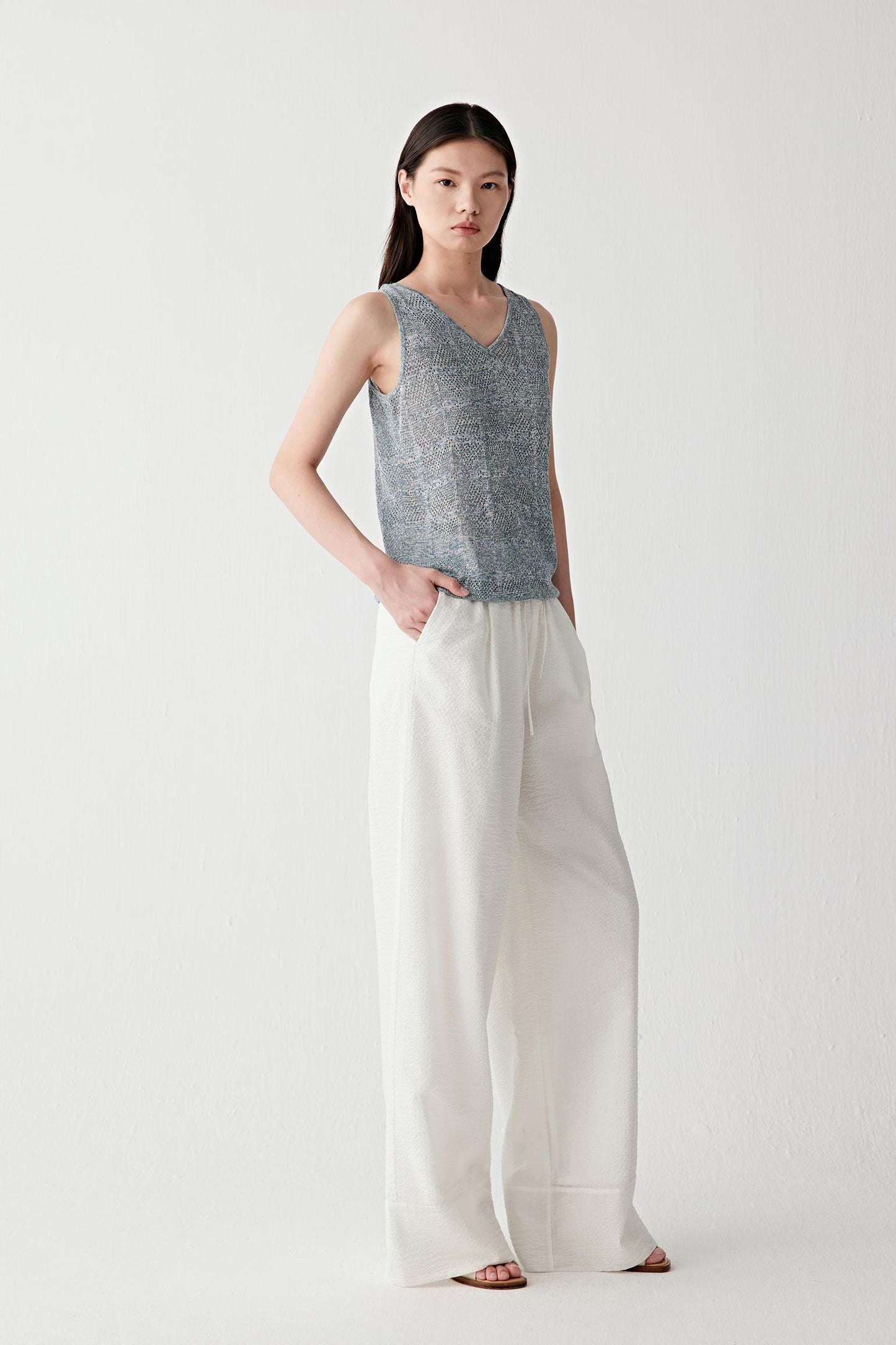 Full-length front view showing the vest paired with ivory trousers, emphasizing the fitted silhouette, sleeveless construction and fluid drape created by the lightweight knit fabric