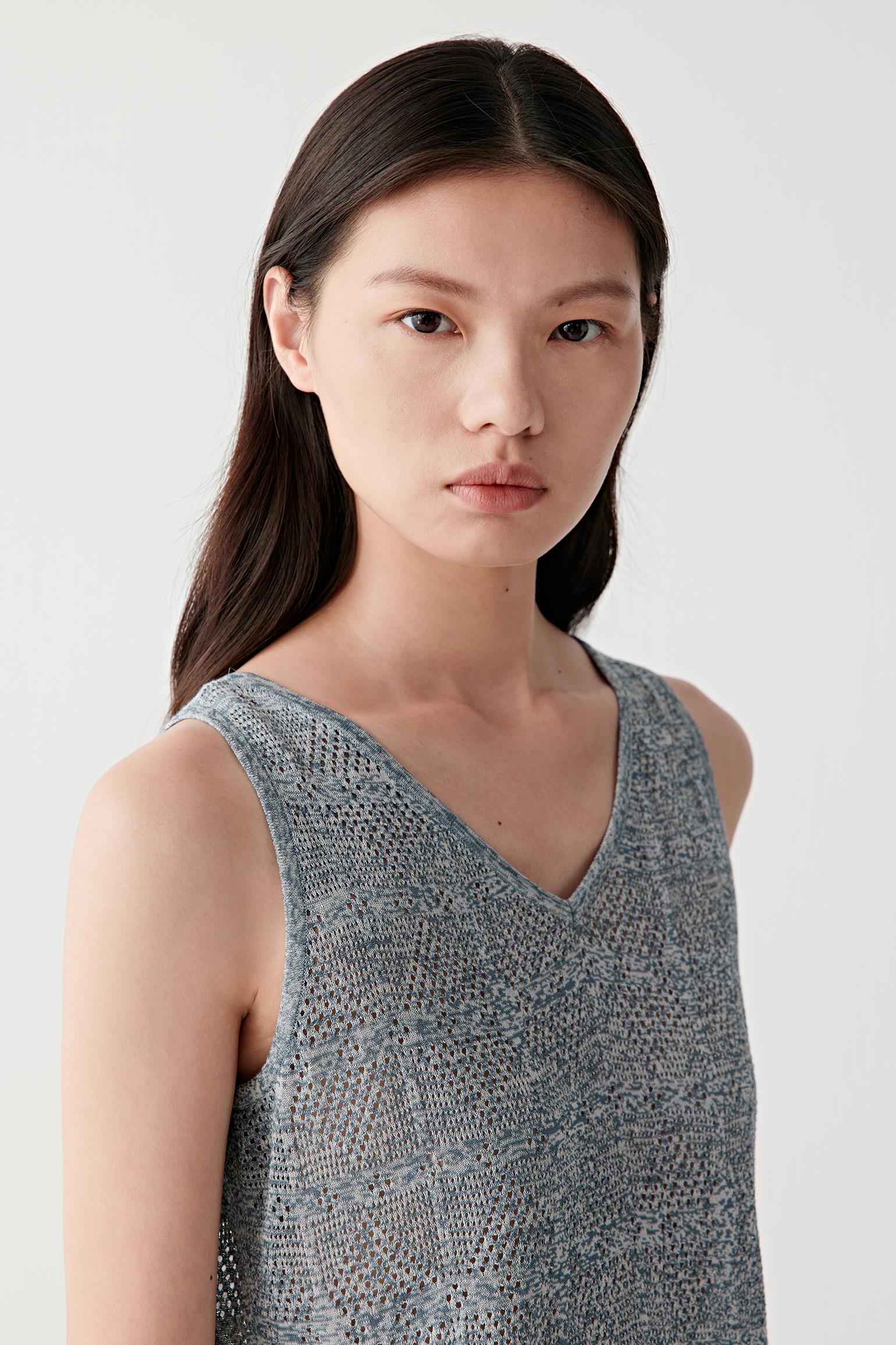 Close-up portrait focusing on the V neckline and upper knit structure, detailing the geometric openwork pattern, grey melange yarn texture and softly textured surface
