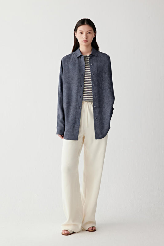 Full-length front view emphasizing the elongated cut, relaxed fit and fluid movement of the shirt, with the indigo blue tone showing subtle tonal variation and a smooth matte surface