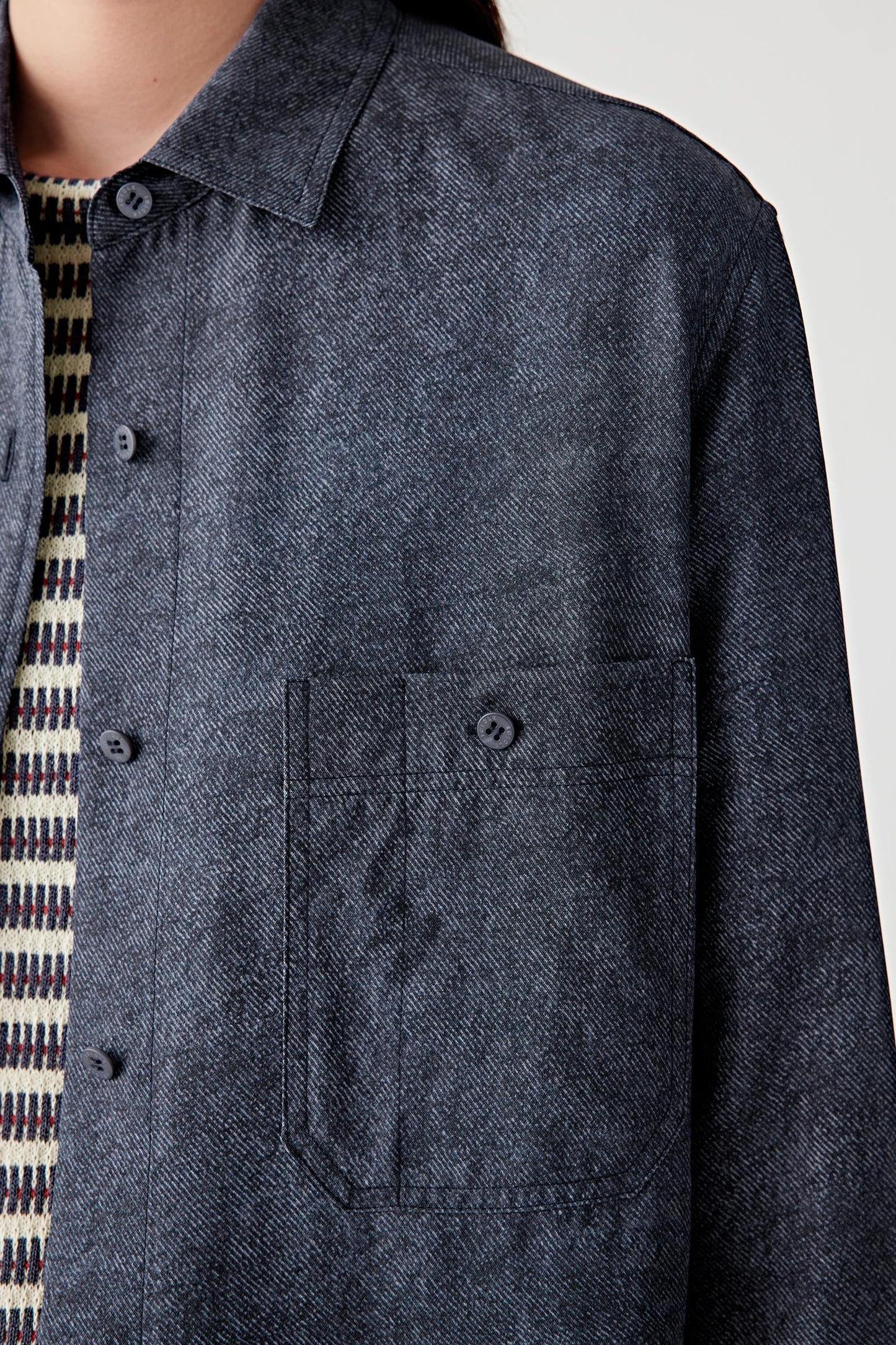 Close-up portrait focusing on the collar, front placket and silk twill texture, detailing the smooth surface, subtle diagonal weave and softly flowing structure of the indigo blue fabric