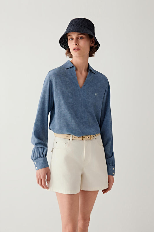 Full-length front view of a woman standing facing forward wearing a light blue shirt and off-white shorts, styled with a slim light beige calf leather belt at the waist, showing the narrow width, smooth leather surface and how the belt subtly structures the silhouette with a clean, minimal line