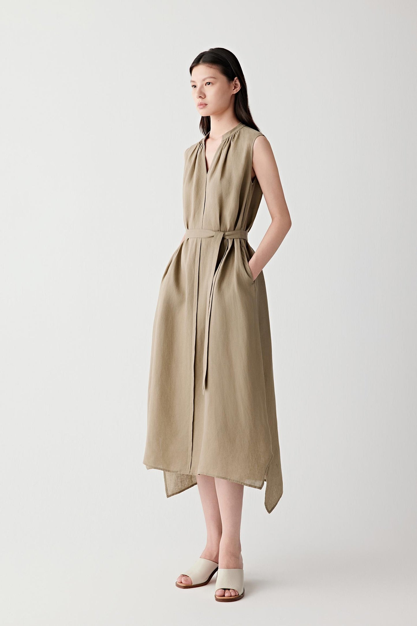 Three-quarter view showing the full length of the dress and the way the lightweight linen drapes through the body. The image emphasizes the defined waist, fluid skirt and subtle irregular texture characteristic of linen.