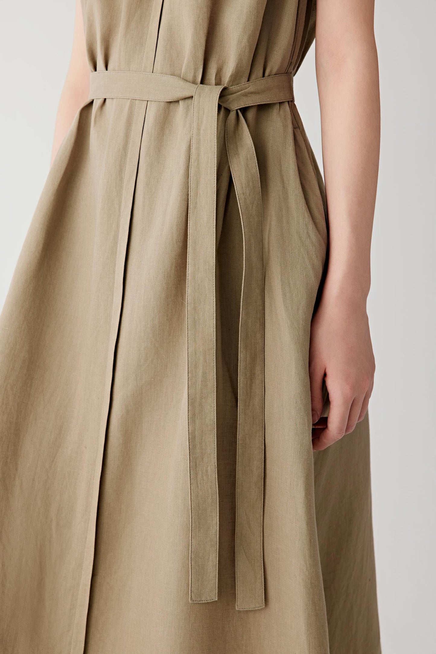 Close-up of the self-tie belt, side pocket and skirt construction. The image highlights the visible linen grain, lightly textured surface and fluid drape of the fabric, revealing the natural character and understated structure of the garment.