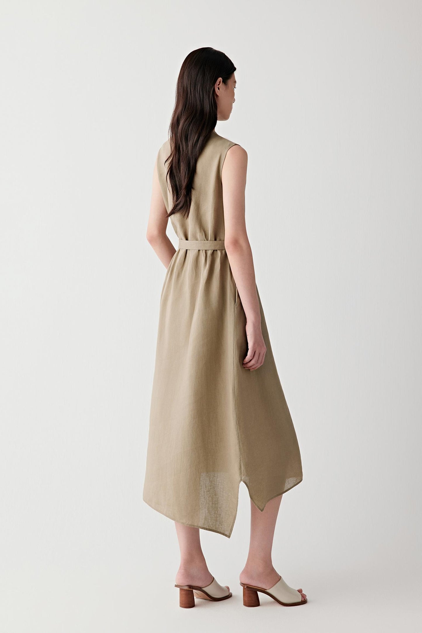Side view highlighting the sleeveless construction, gathered neckline and asymmetric hemline. The lightweight linen fabric falls naturally from the waist, creating soft movement and a relaxed silhouette.