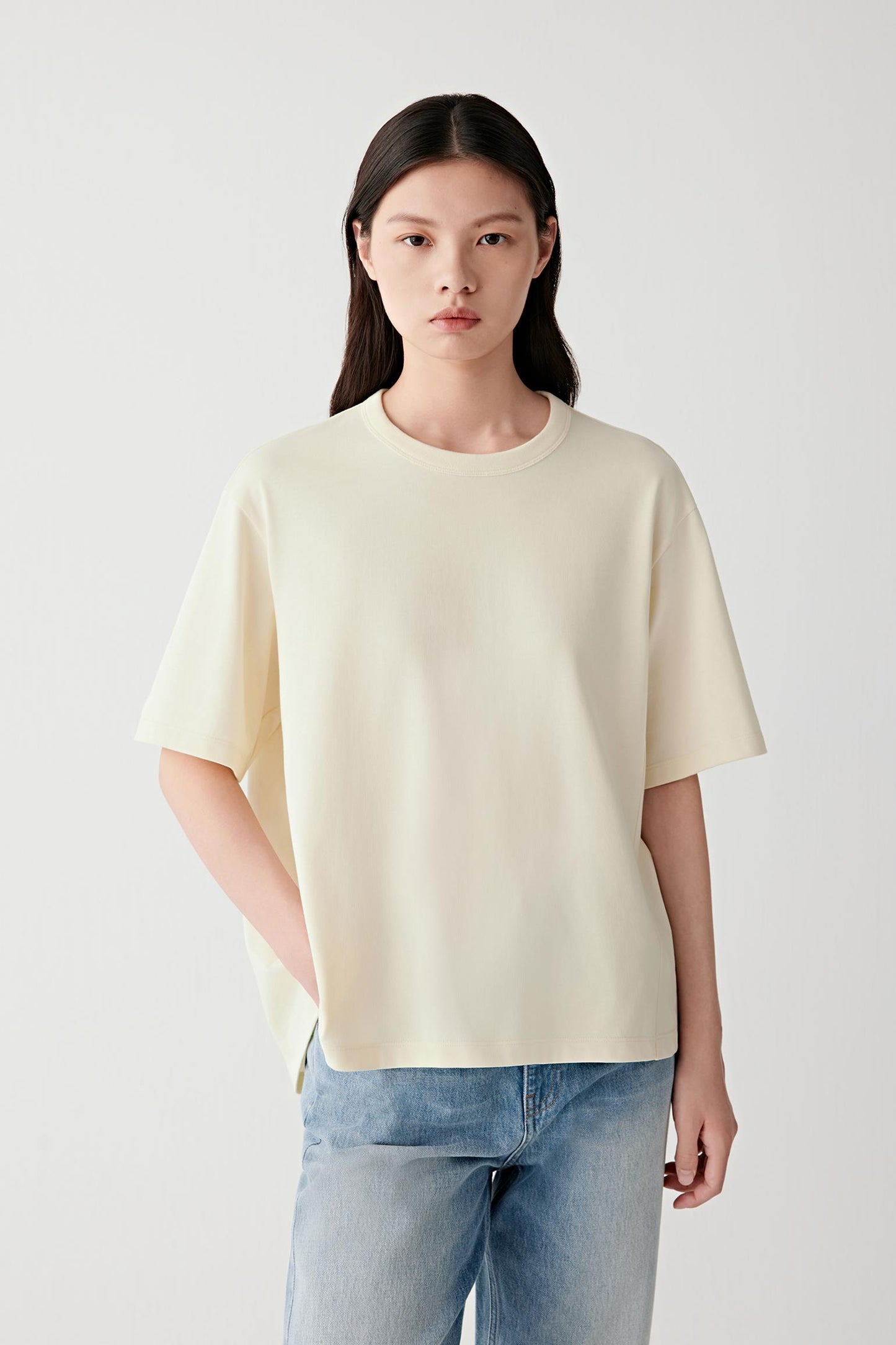Front view of a woman wearing a pale yellow cotton jersey T-shirt, highlighting the relaxed silhouette, smooth surface and soft hand of the fabric. The straight cut and clean construction create an understated everyday silhouette with balanced proportions.