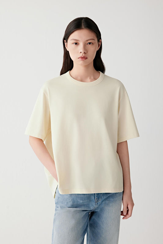 Front view of a woman wearing a pale yellow cotton jersey T-shirt, highlighting the relaxed silhouette, smooth surface and soft hand of the fabric. The straight cut and clean construction create an understated everyday silhouette with balanced proportions.