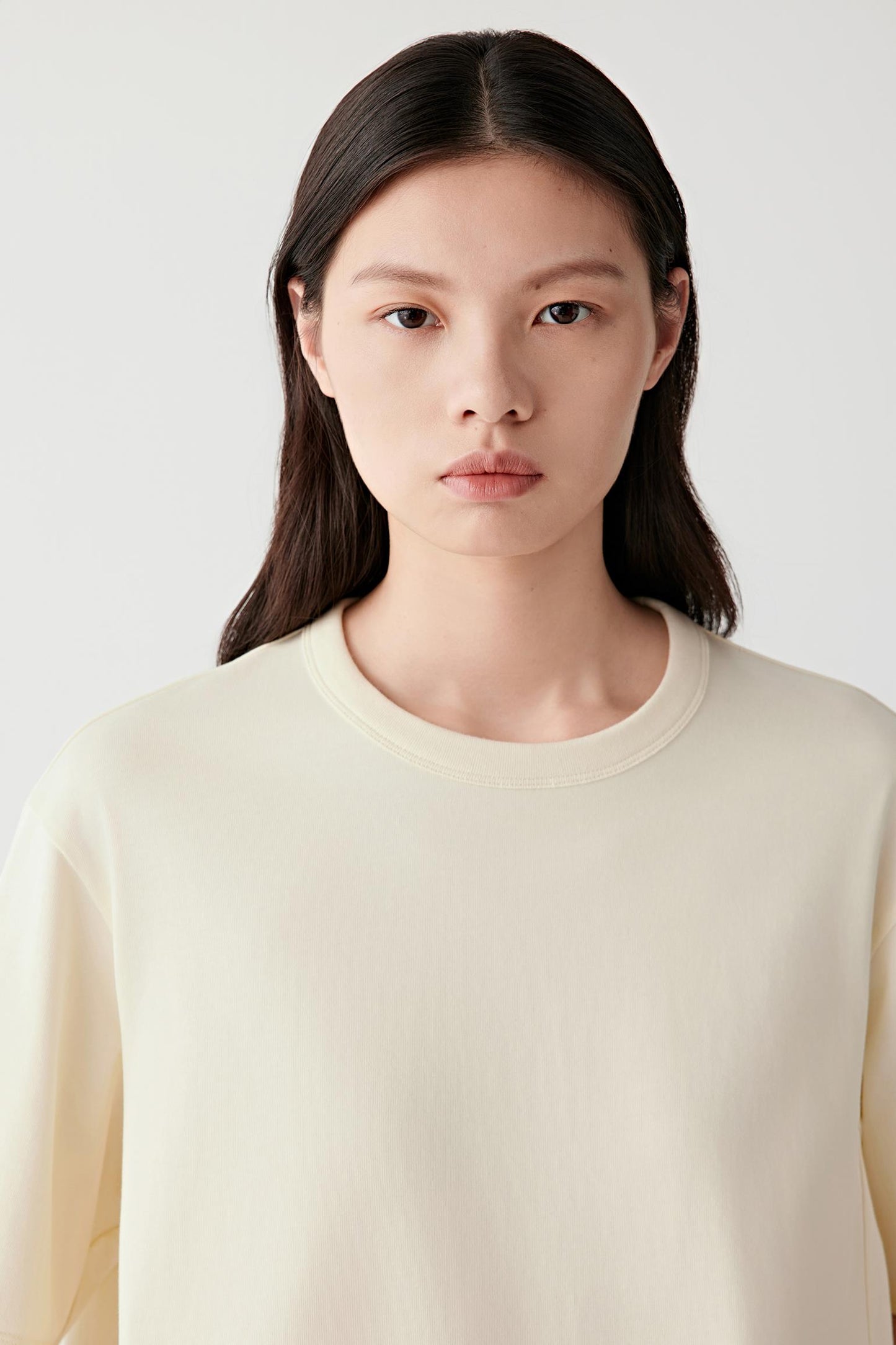 Close-up portrait focusing on the round neckline with ribbed trim and the upper body construction. The image highlights the clean finishing, smooth texture and soft appearance of the cotton jersey fabric.
