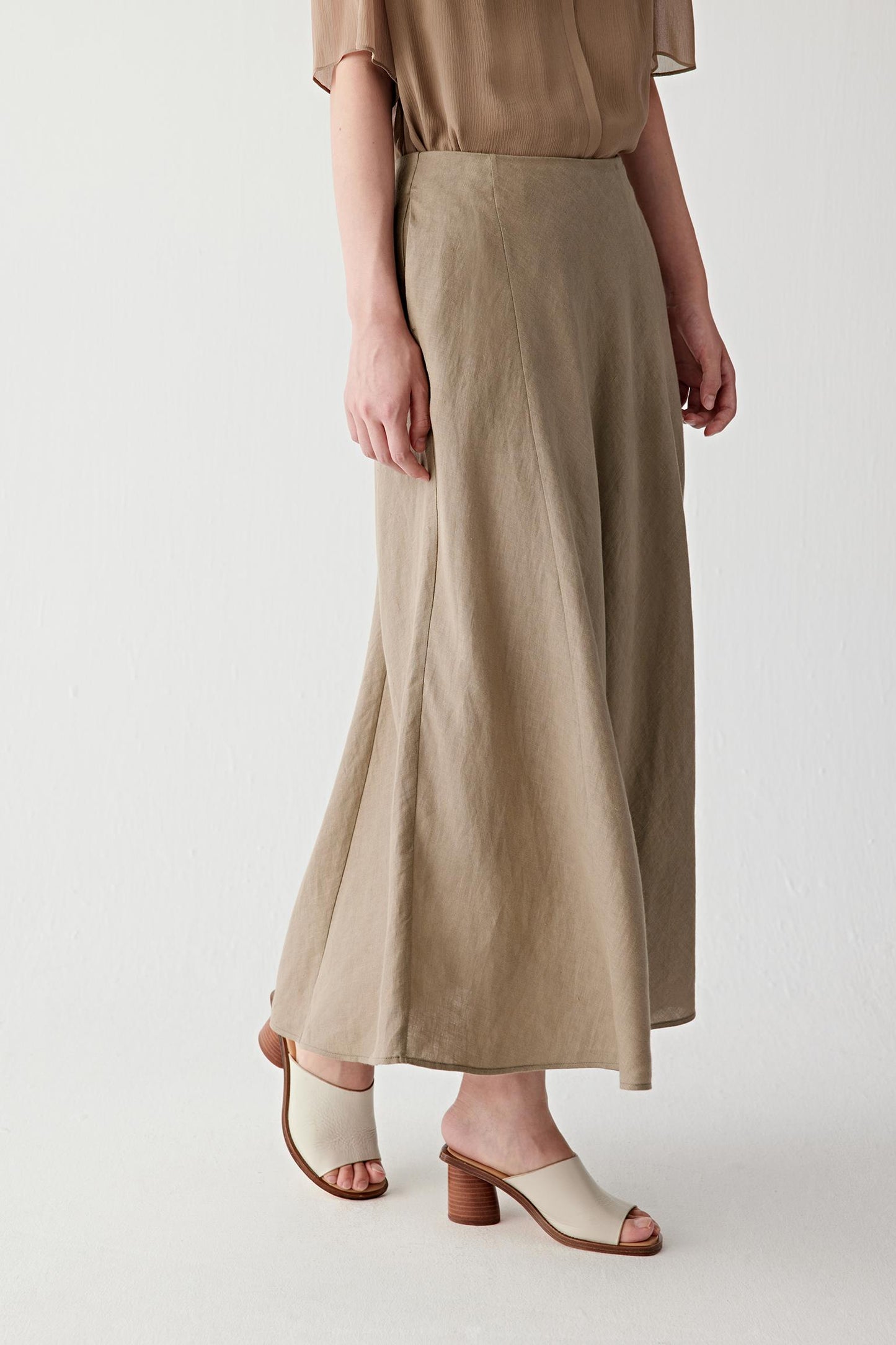 Side view highlighting the panelled construction and the way the skirt falls smoothly from the fitted waistband. The lightweight linen maintains structure while allowing fluid movement through the lower silhouette.