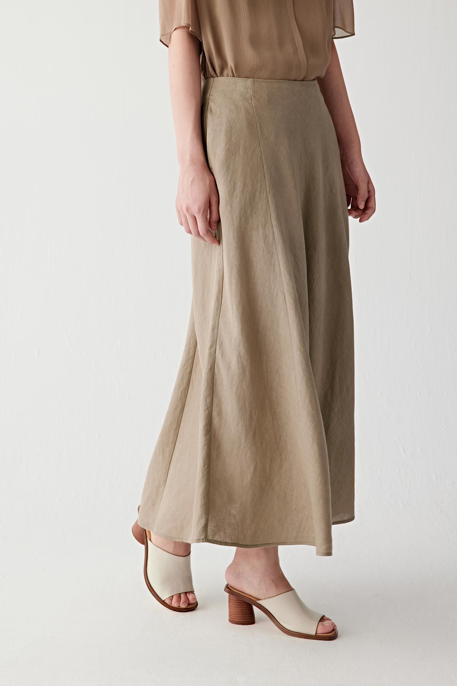 Side view highlighting the panelled construction and the way the skirt falls smoothly from the fitted waistband. The lightweight linen maintains structure while allowing fluid movement through the lower silhouette.