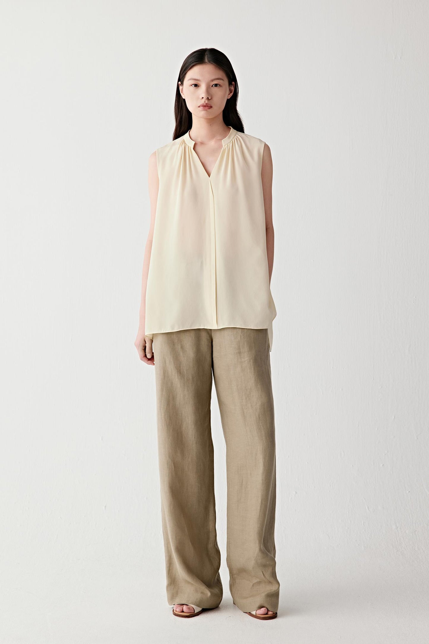 Front view of a woman wearing brown linen trousers, highlighting the straight-leg silhouette, lightweight structure and naturally textured surface. The visible grain of the linen fabric creates subtle tonal variation while maintaining a fluid and relaxed appearance.