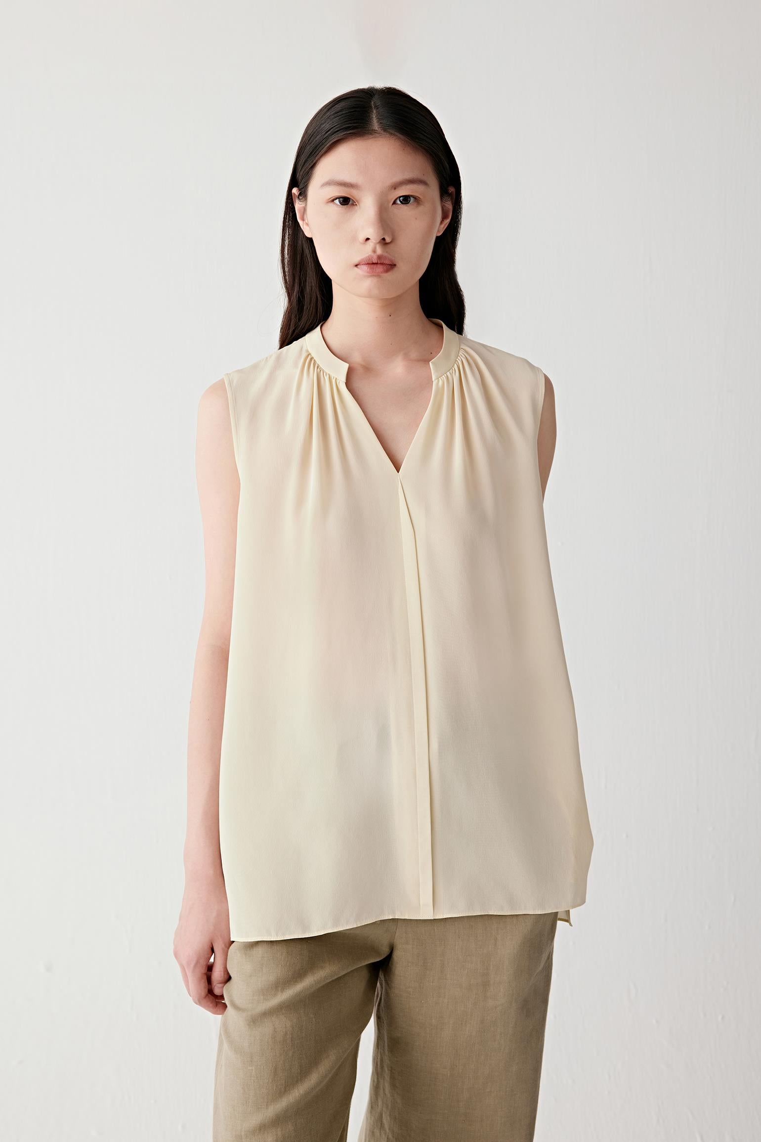 Front view of a woman wearing a pale yellow blouse in silk crêpe de Chine, highlighting the fluid silhouette, soft drape and matte surface of the fabric. The gathered neckline and V-shaped opening create gentle volume through the upper body while maintaining clean, balanced proportions.