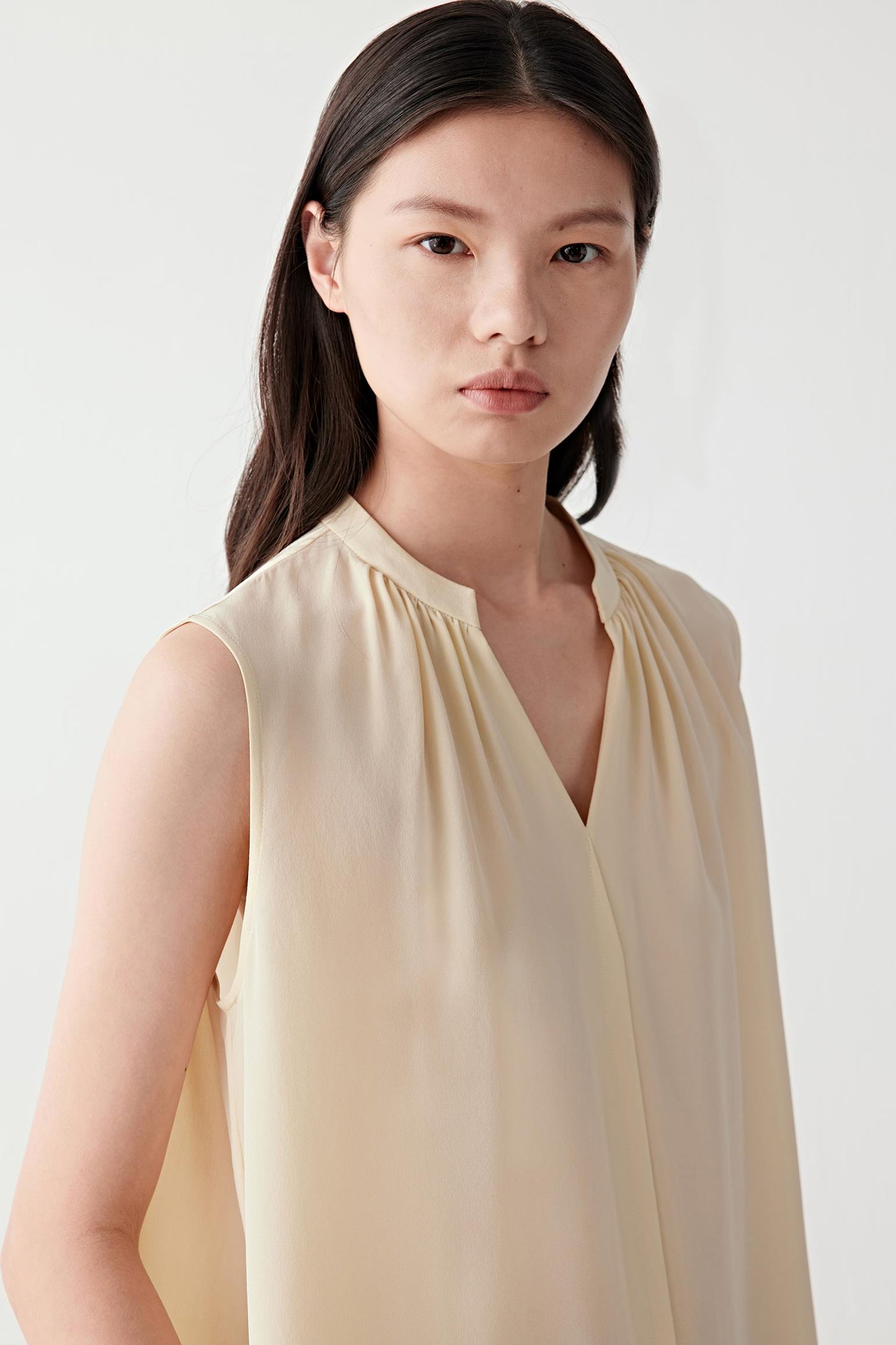 Close-up portrait focusing on the V-shaped neckline, band collar and gathered detailing at the front. The image highlights the smooth surface, soft hand and fluid quality characteristic of silk crêpe de Chine.