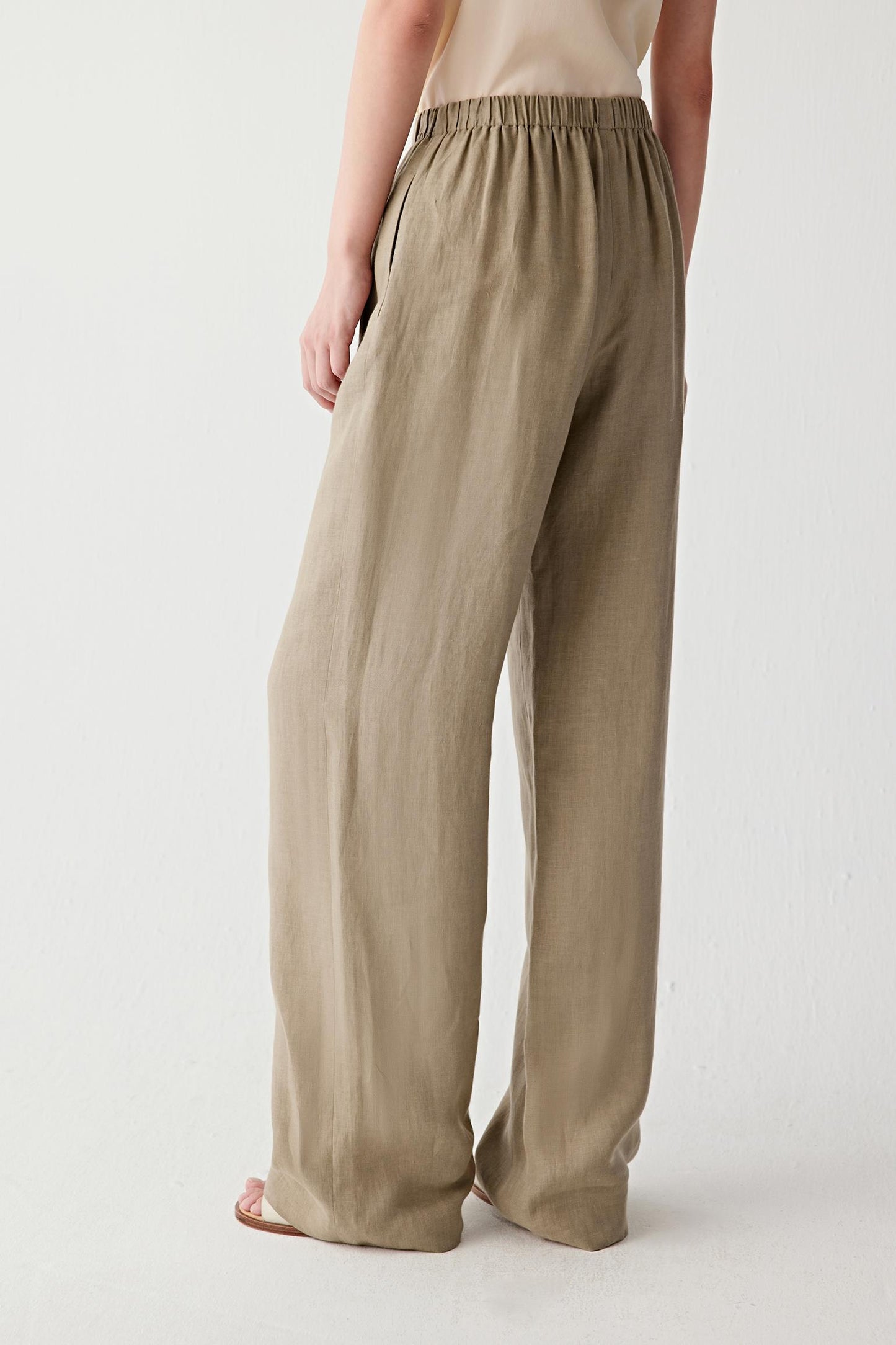 Angled rear view highlighting the volume and drape of the trousers. The image reveals the relaxed structure of the garment and the characteristic texture of the linen weave.