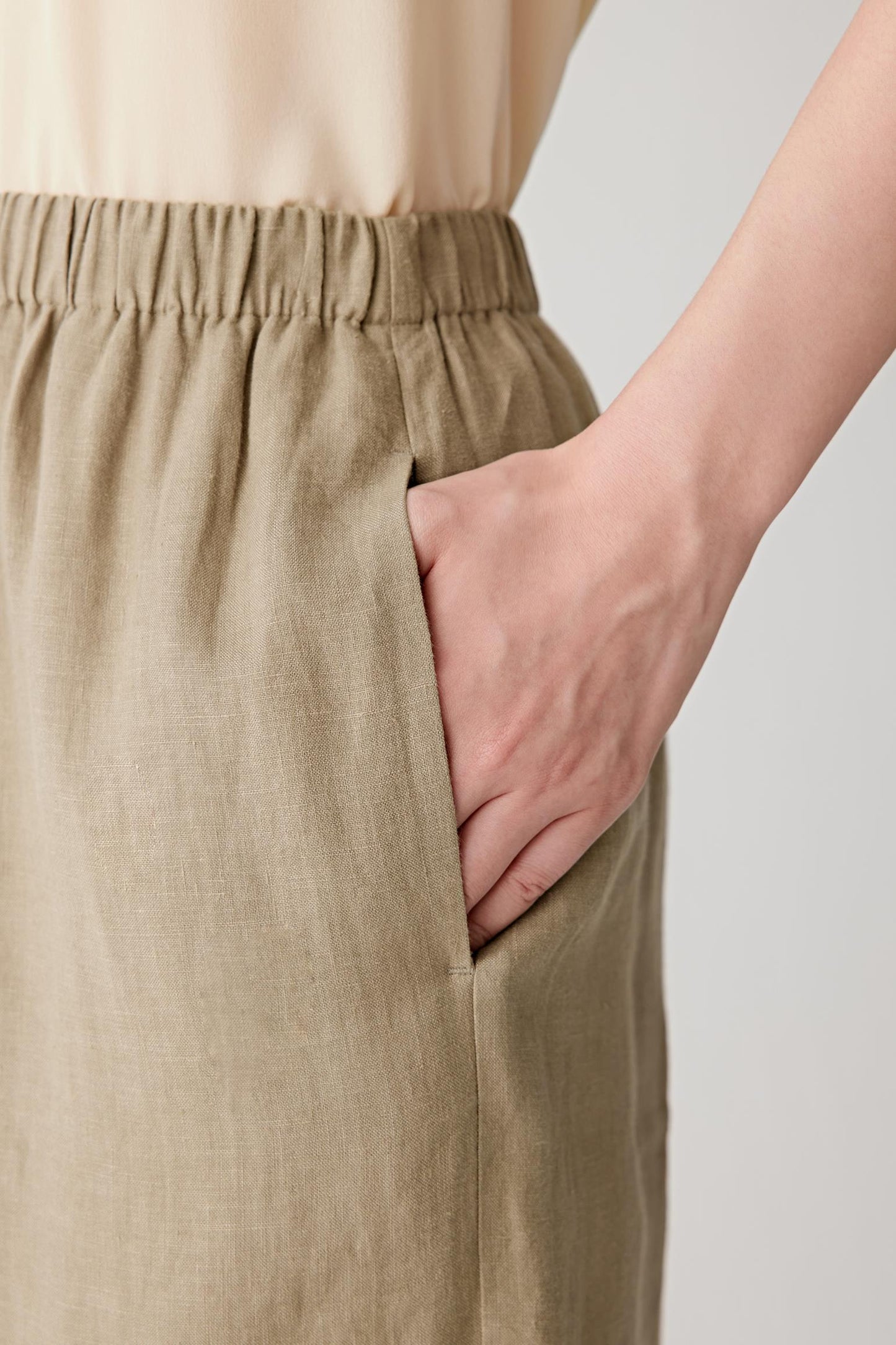 Close-up of the elasticated drawstring waistband and side pocket construction. The image highlights the visible linen grain, natural irregular texture and the soft drape of the lightweight fabric.