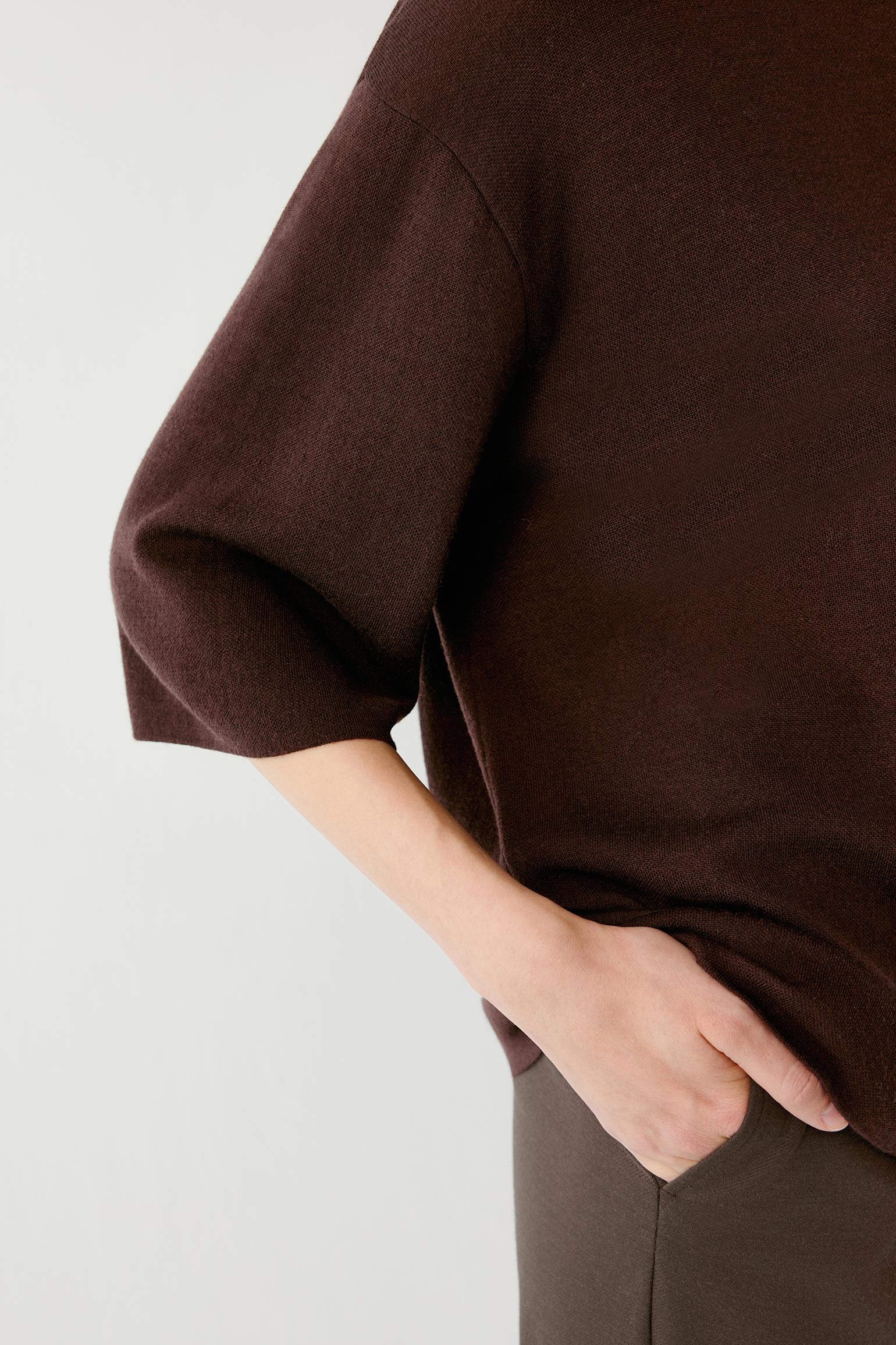 Close-up of a person wearing a dark brown knit top with elbow-length sleeves and a relaxed fit, paired with brown bottoms against a plain light background.