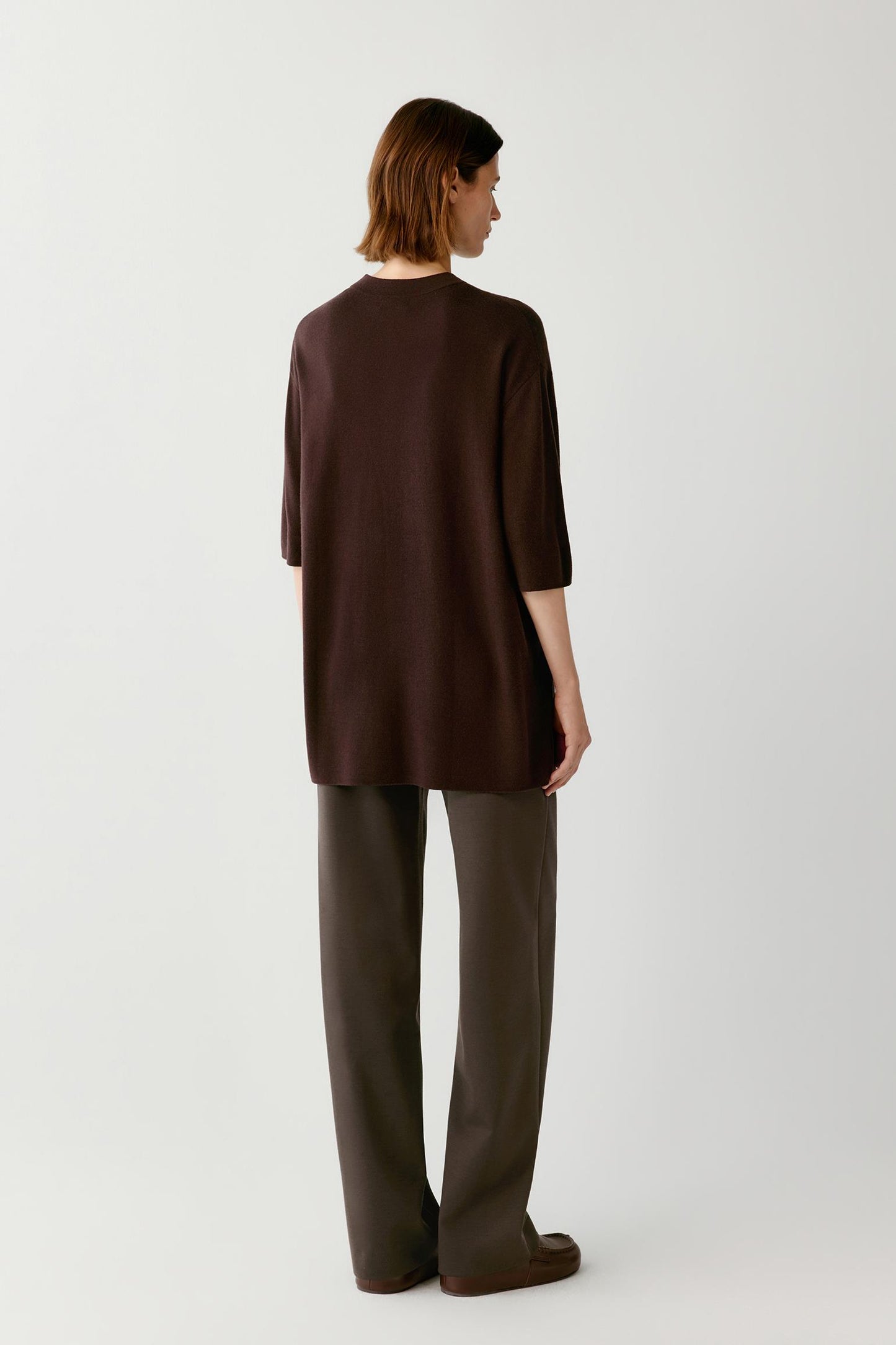 A model shown from the back wearing a dark brown short-sleeve top and matching dark brown wide-leg trousers against a light gray studio background.