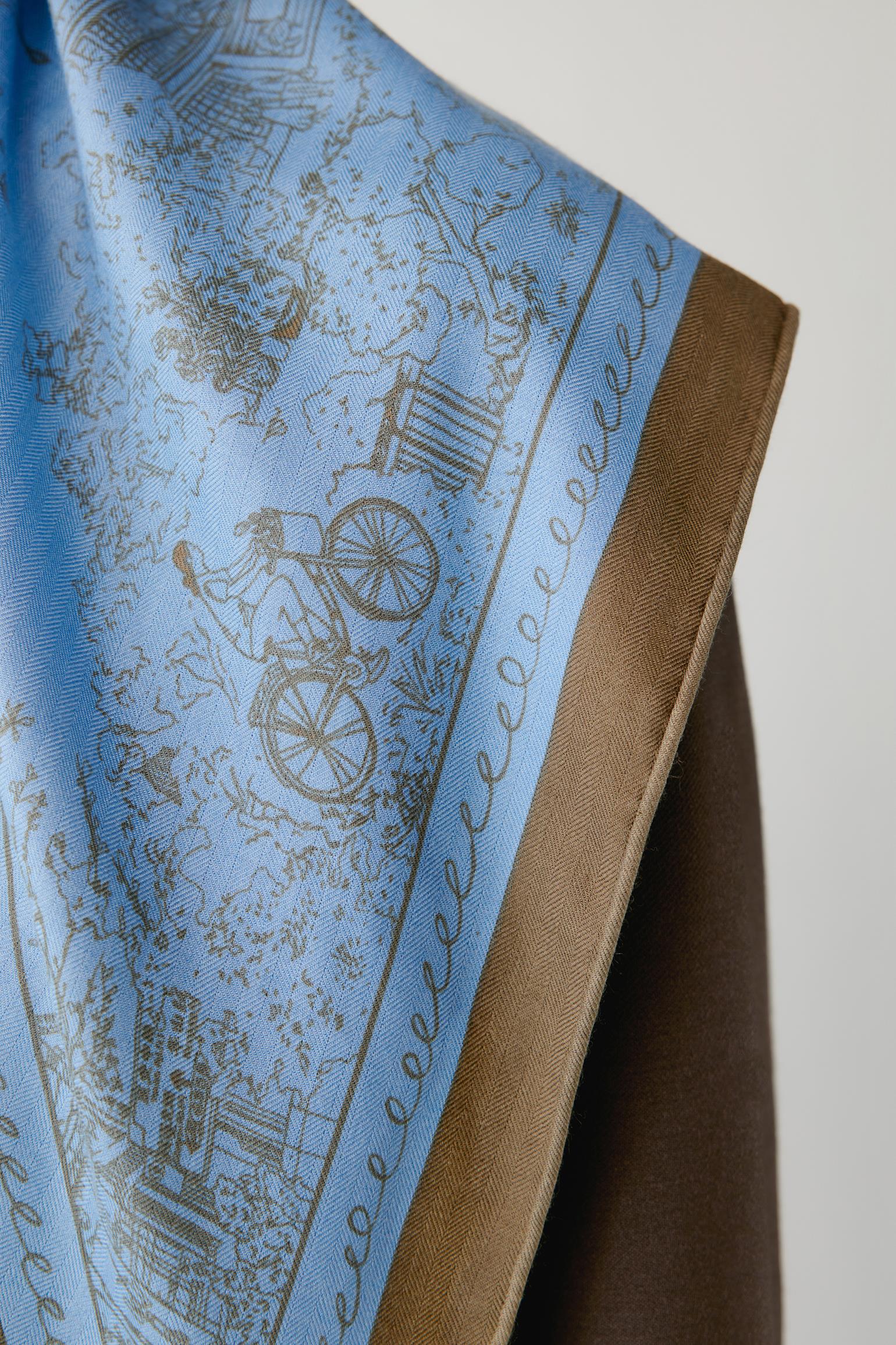 Close-up of a blue scarf with brown illustrated motifs and a contrasting brown border.
