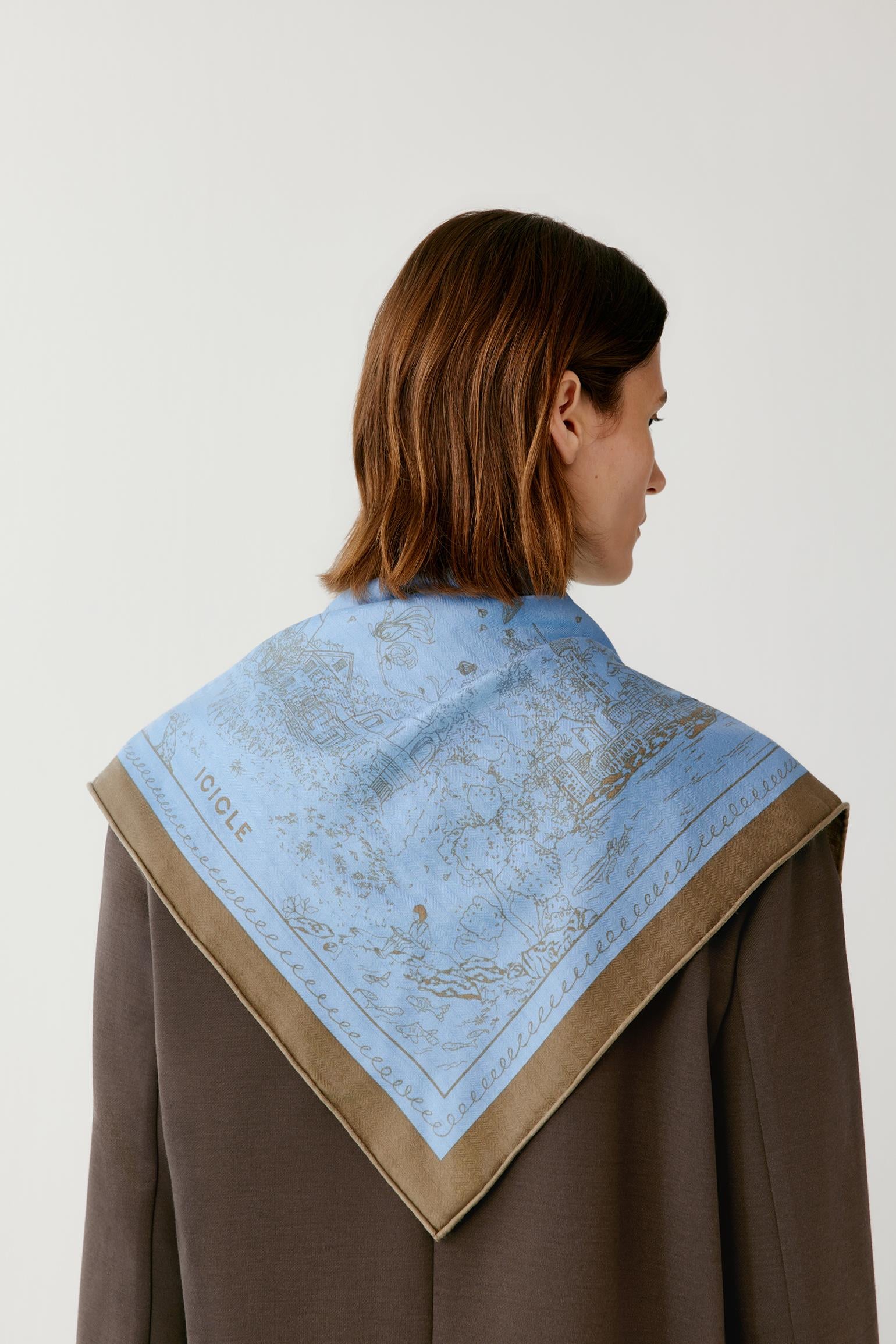 Back view of a woman wearing a blue patterned scarf over a brown blazer.