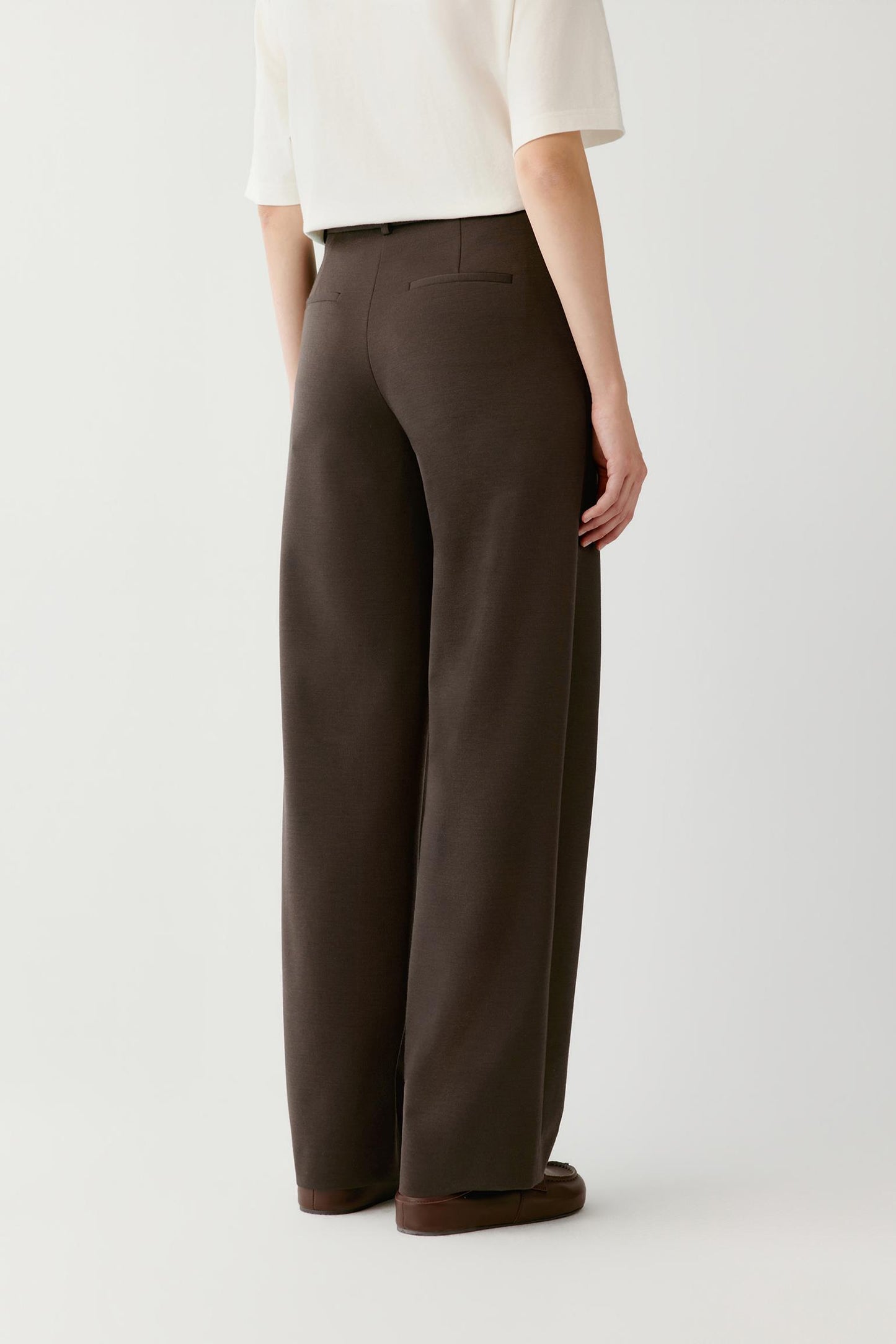 Back view of a woman wearing brown wide-leg tailored trousers with a white top.