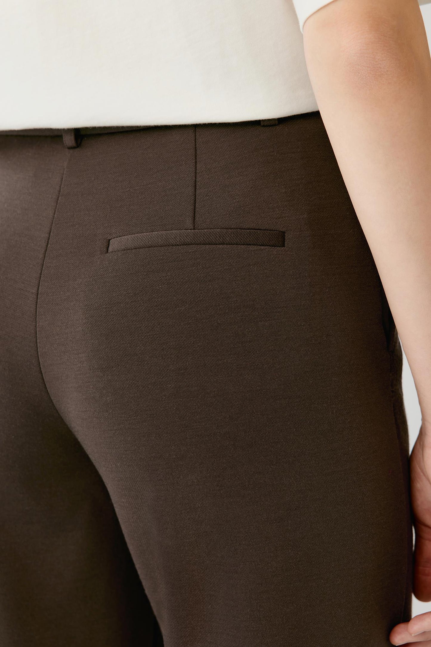Close-up of the back welt pocket and textured fabric of brown tailored trousers.