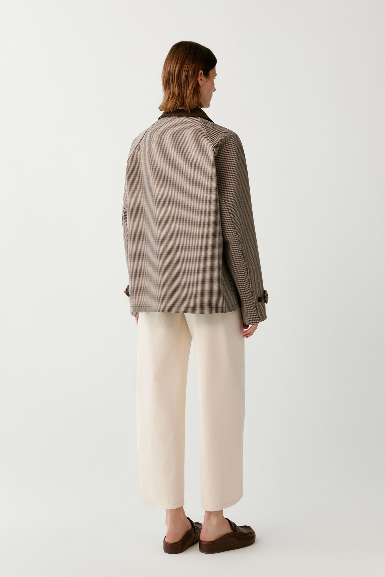 A model shown from the back wearing a taupe-brown textured jacket, cream wide-leg trousers, and brown leather loafers against a plain white studio background.