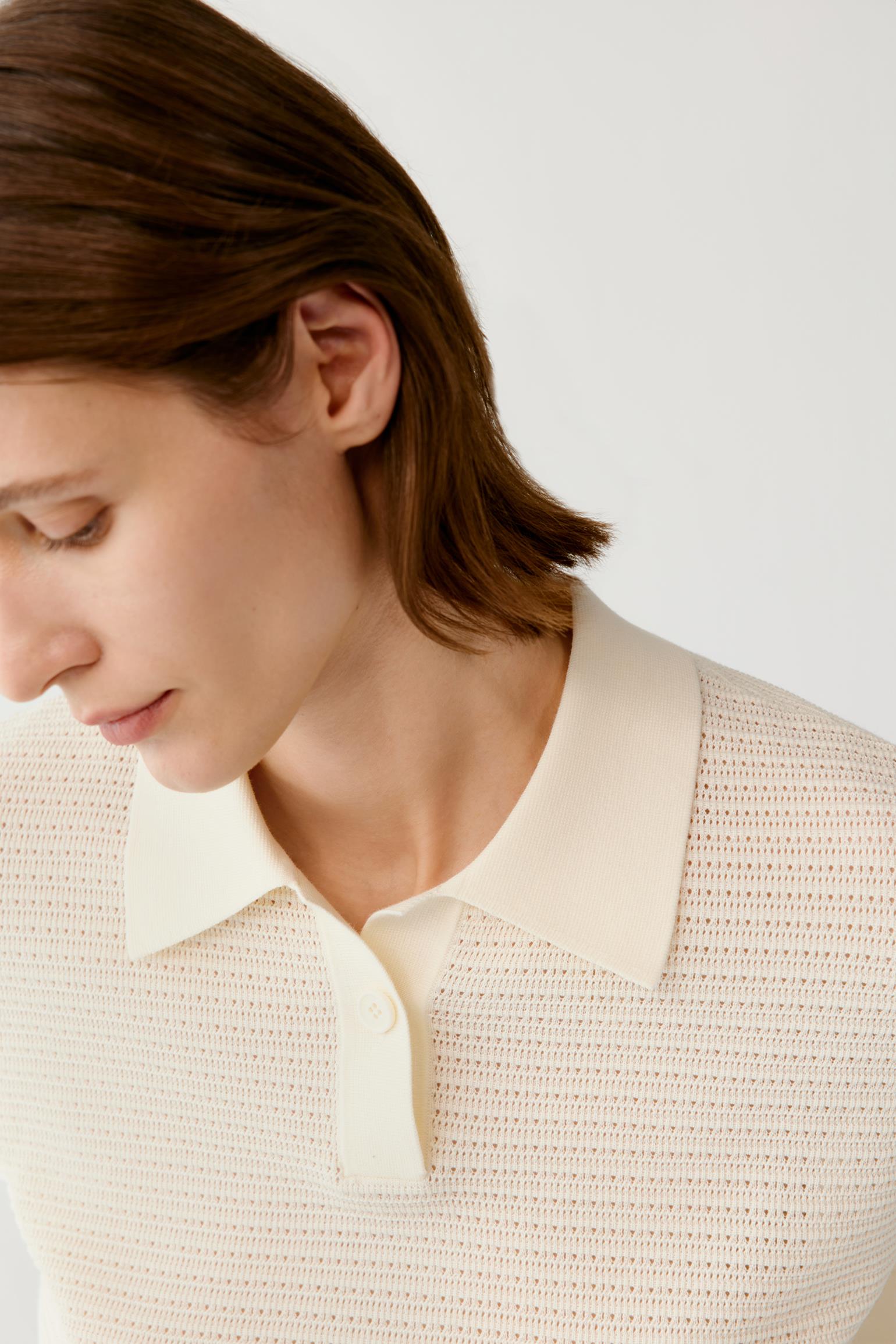 Close-up of a model wearing a cream-colored textured knit polo shirt with a solid collar, set against a plain light gray background.