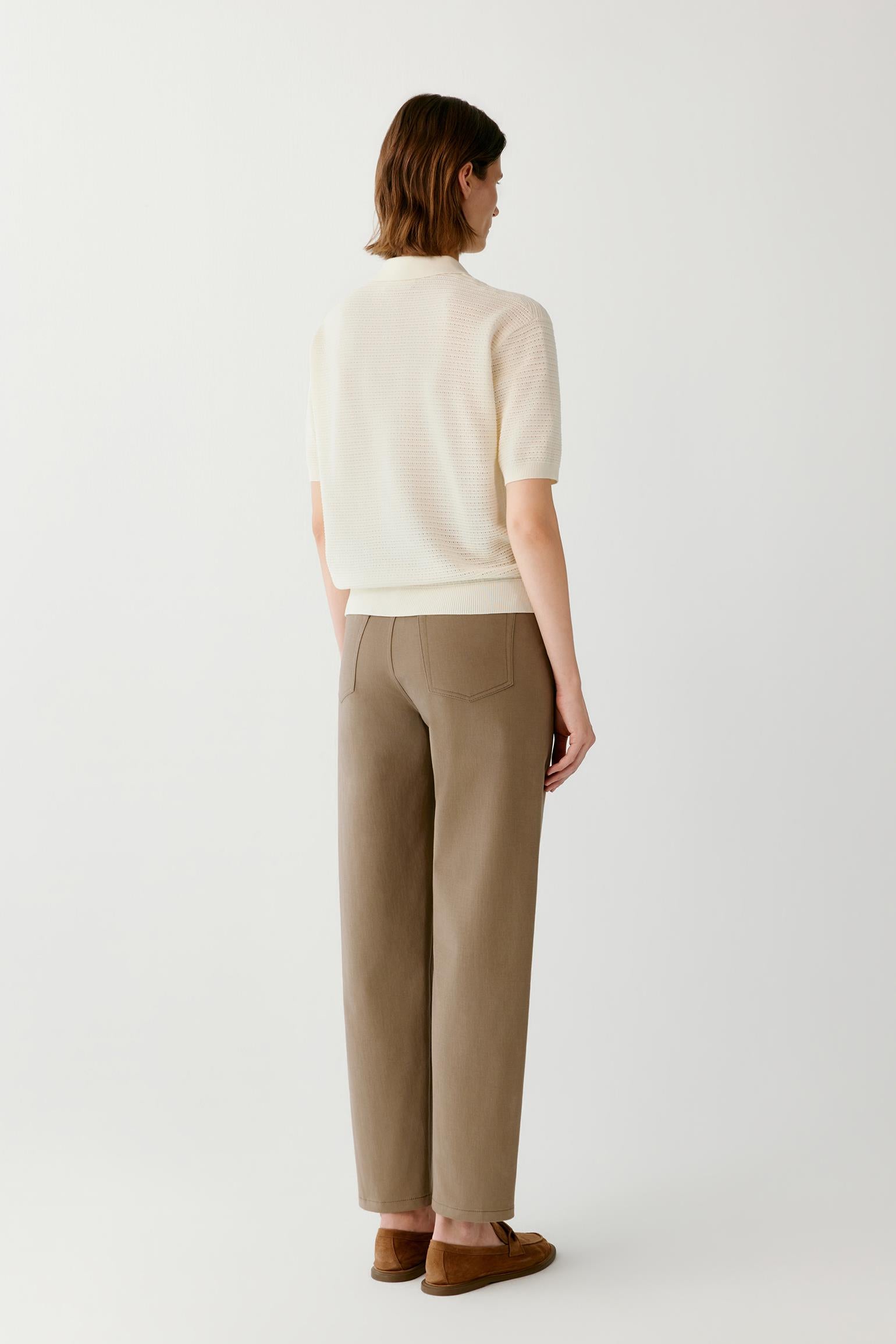 A model shown from the back wearing a cream short-sleeve knit top, beige wide-leg trousers, and brown suede loafers, set against a plain light gray studio background.