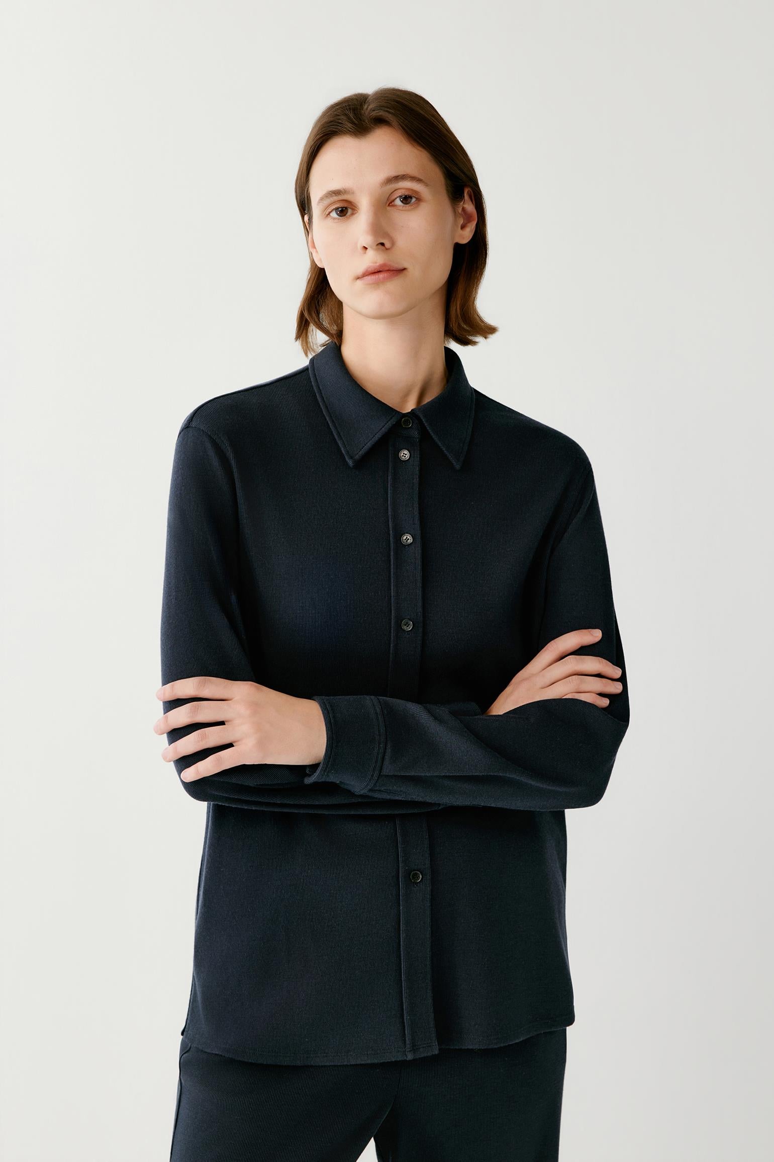 Woman wearing a textured navy button-up shirt with her arms crossed.