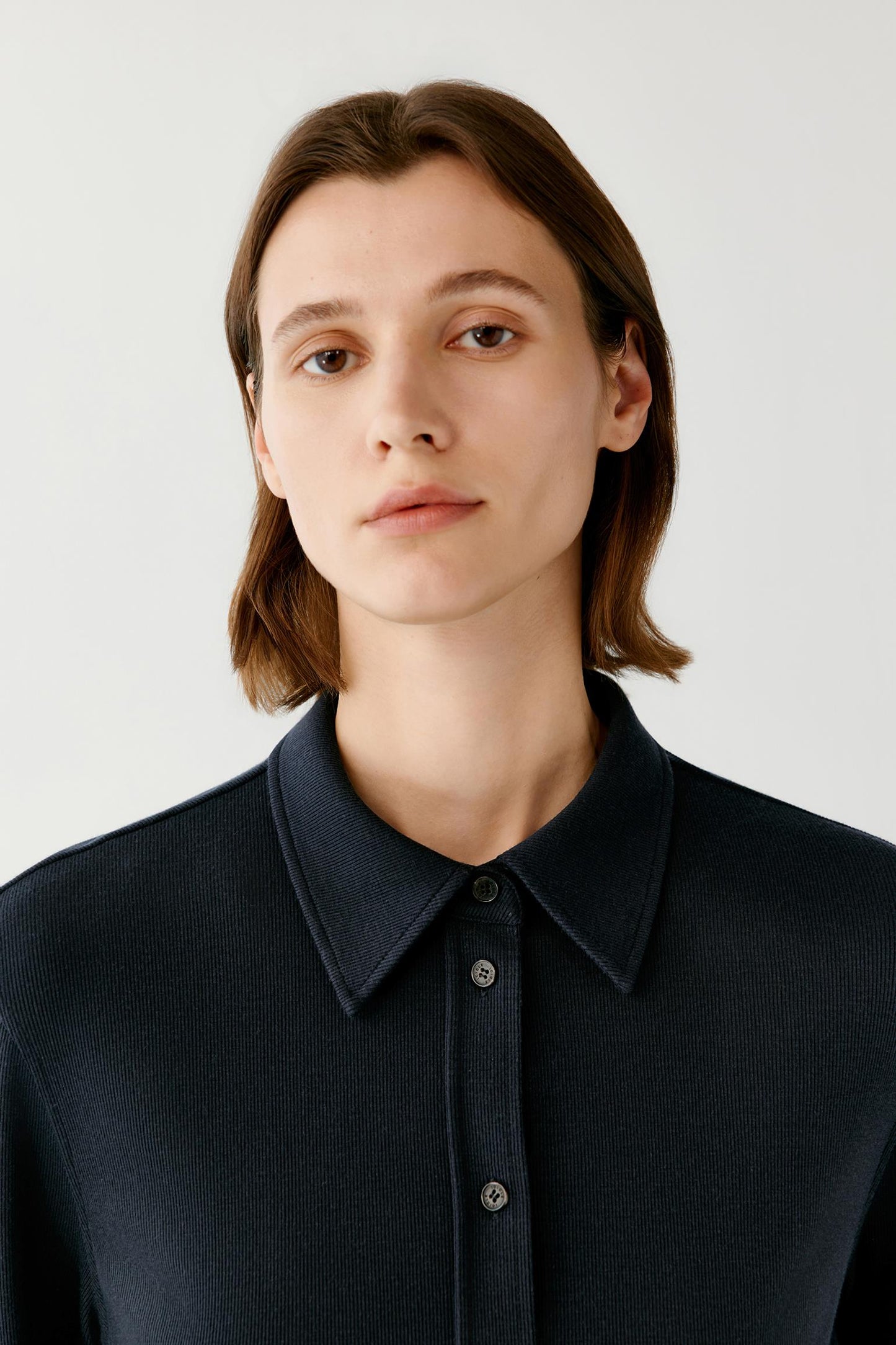 Close-up of a woman wearing a textured navy collared shirt.