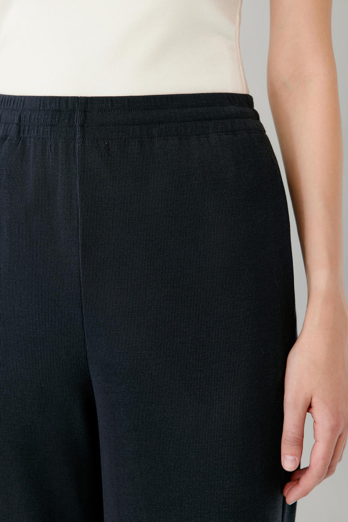Close-up of a person wearing dark navy wide-leg pants with an elastic waistband, paired with a light cream top against a neutral gray background.