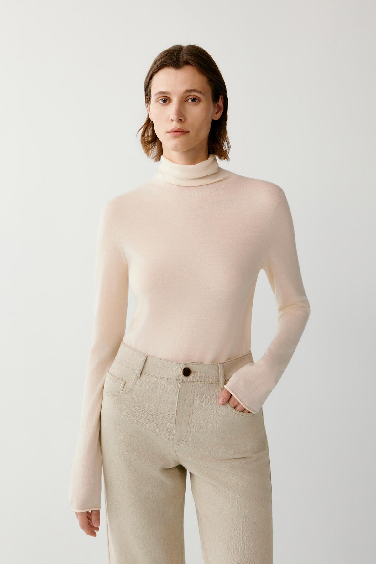 Front view highlighting the turtleneck, long sleeves and smooth knit texture of the cream wool and cashmere pullover.