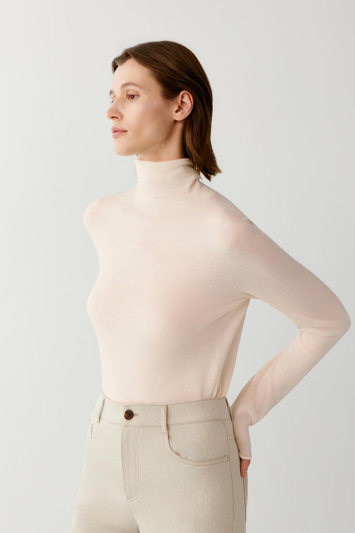 Side view of a woman wearing the cream wool and cashmere pullover, highlighting the fitted shape and long sleeves.