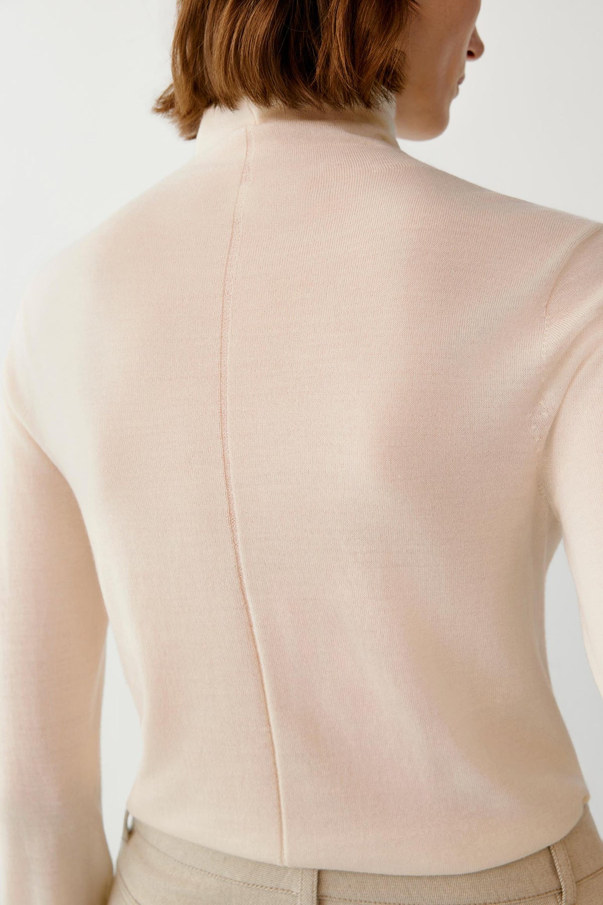 Close-up of the back highlighting the turtleneck and smooth cream knit surface.