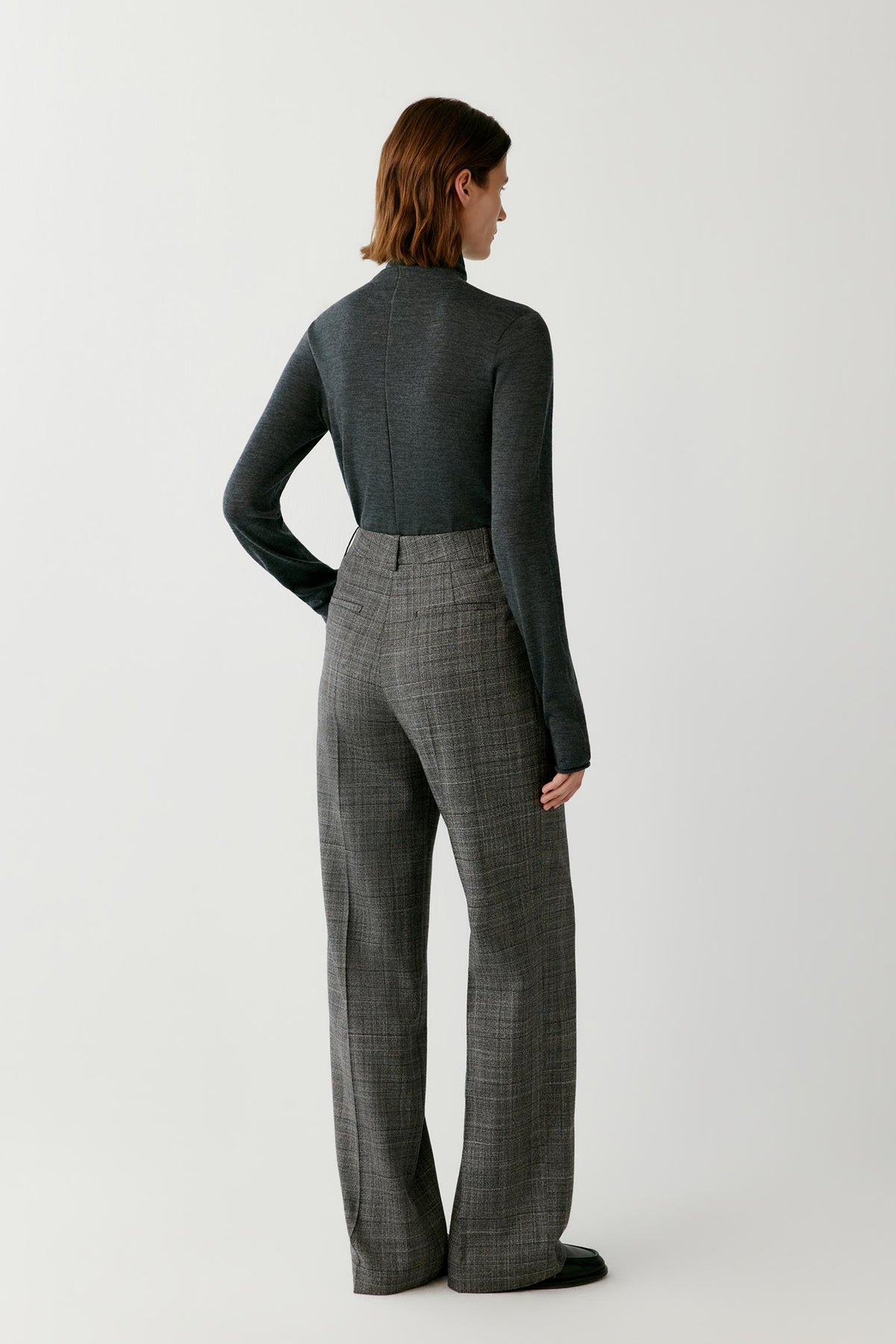 Back full-length view of a woman wearing the dark grey wool and cashmere pullover, showing the turtleneck and straight silhouette.