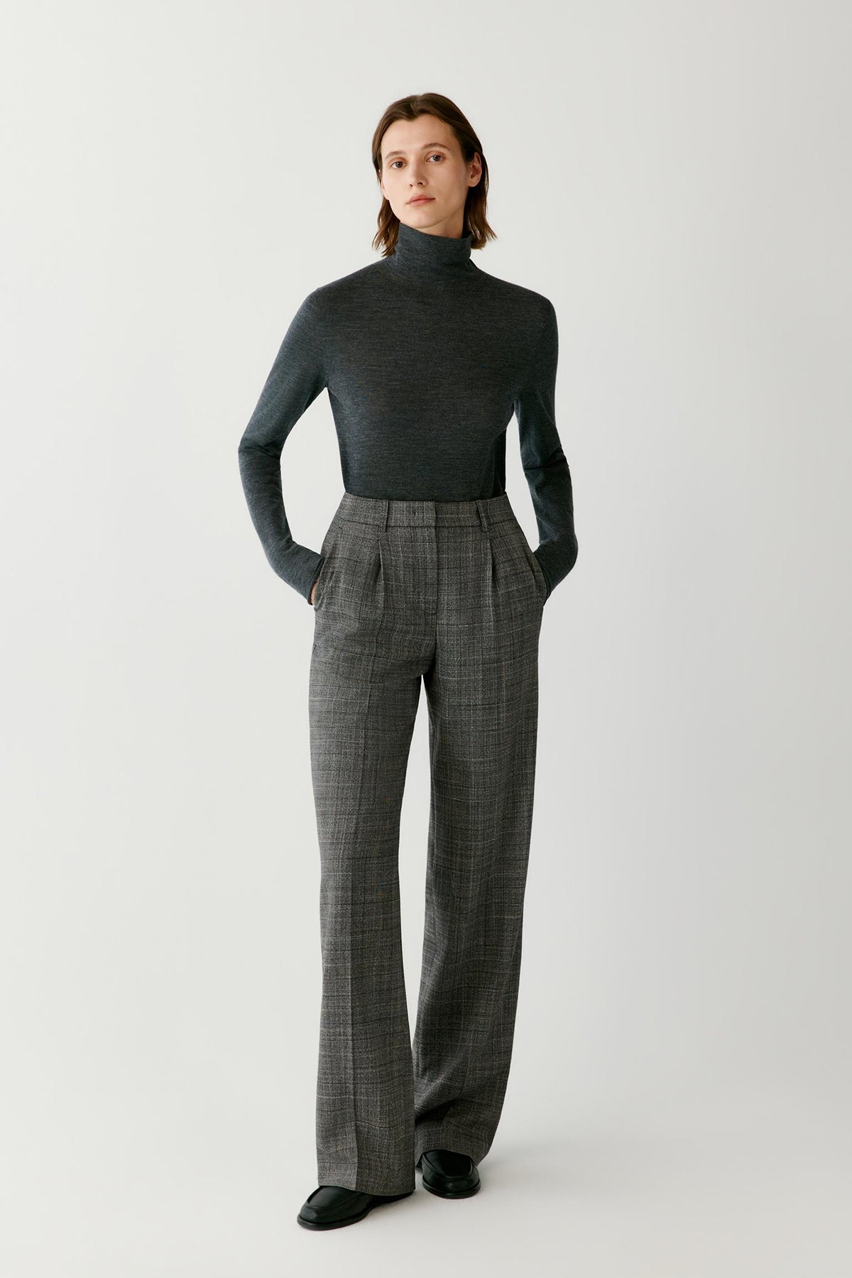 Front full-length view of a woman wearing the dark grey wool and cashmere pullover, highlighting the turtleneck and fitted silhouette.