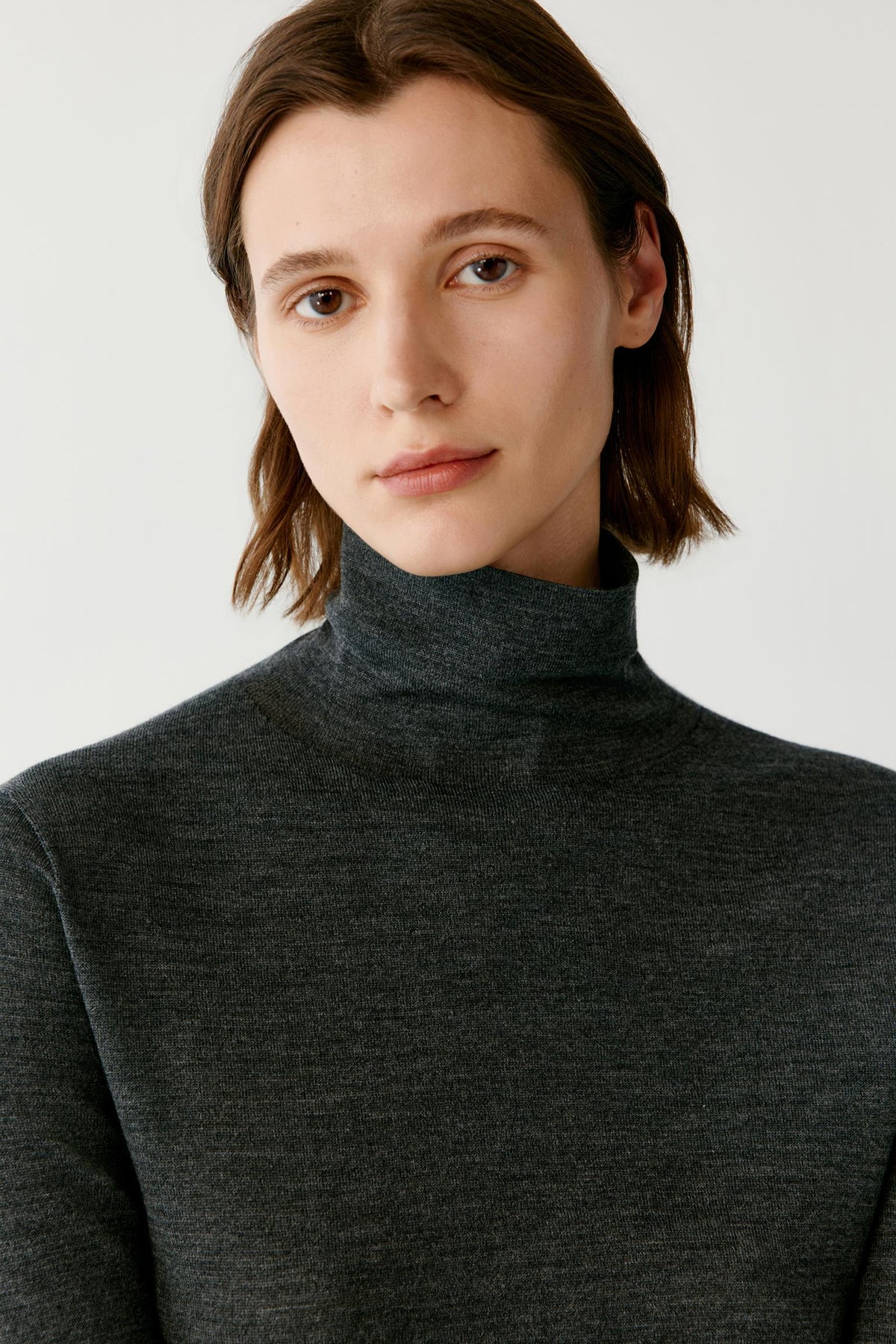 Close-up highlighting the turtleneck and smooth fine-knit texture of the dark grey wool and cashmere pullover.