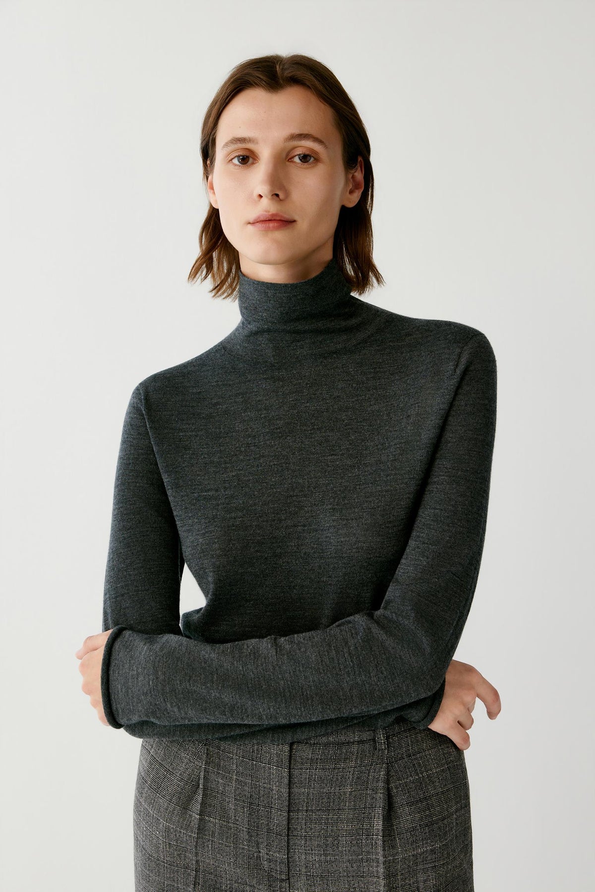 Front view of a woman wearing a dark grey wool and cashmere pullover, showing the turtleneck, long sleeves and straight silhouette.