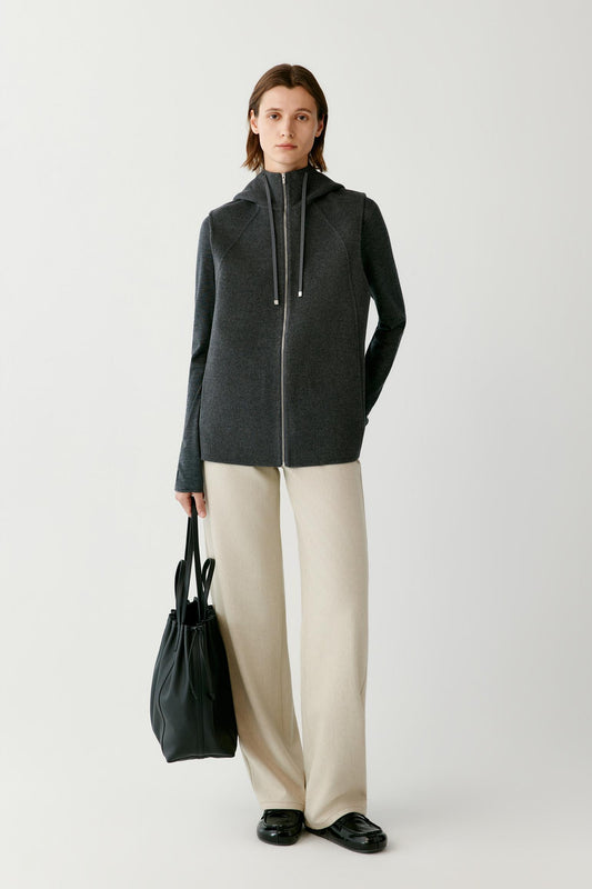 Front view of a woman wearing a dark grey melange sleeveless wool and cashmere coat, showing the hood, zip front and straight silhouette.