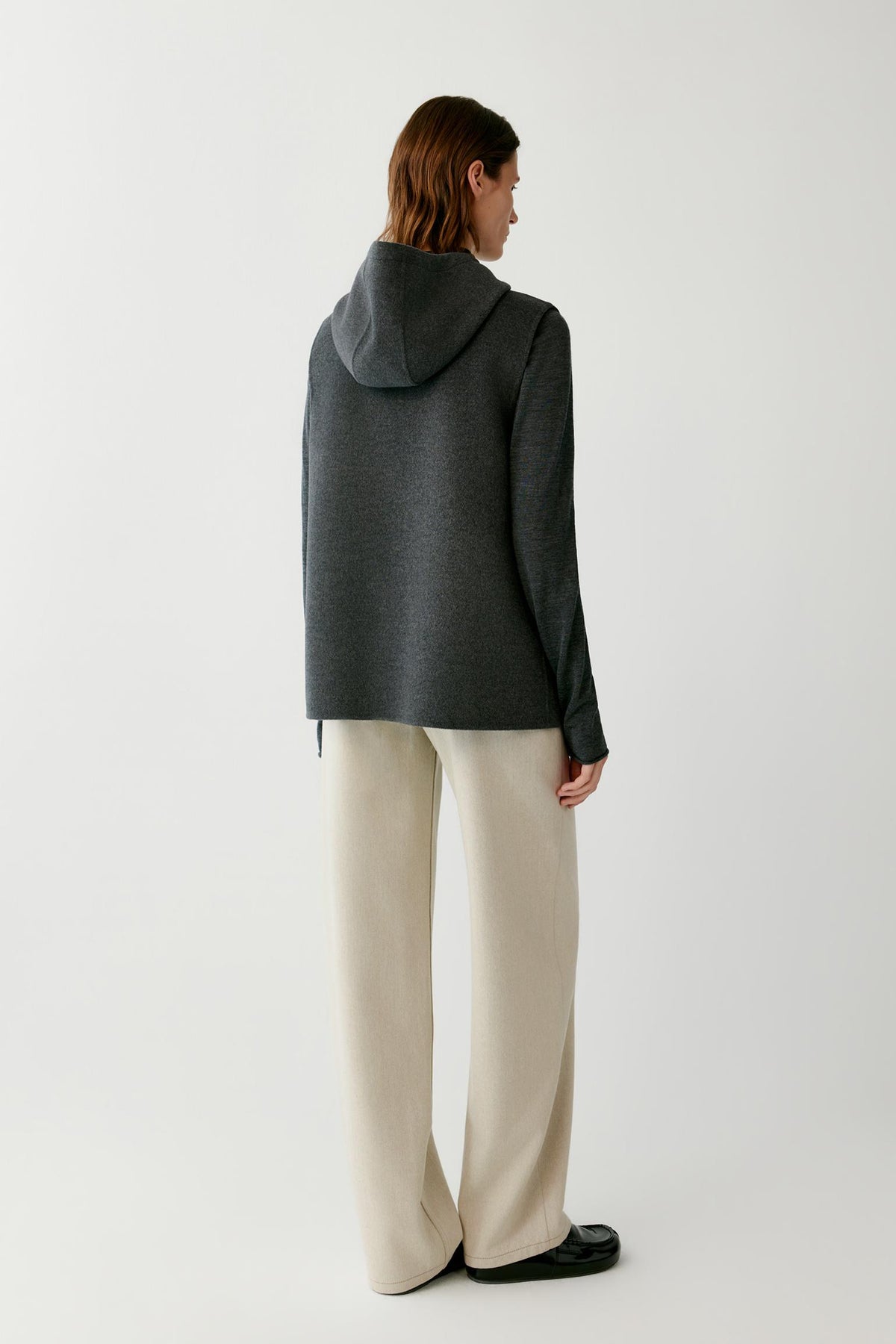 Back view of a woman wearing the dark grey melange sleeveless coat, showing the hood and straight silhouette.